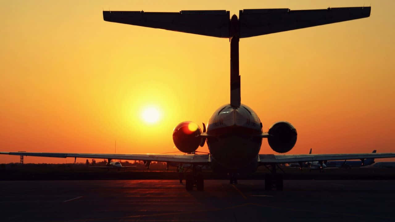 欣賞壯麗的天空全景 壁紙 — 一架雙引擎飛機在機場停機坪上，以鮮豔的橙色日落為背景呈現剪影。