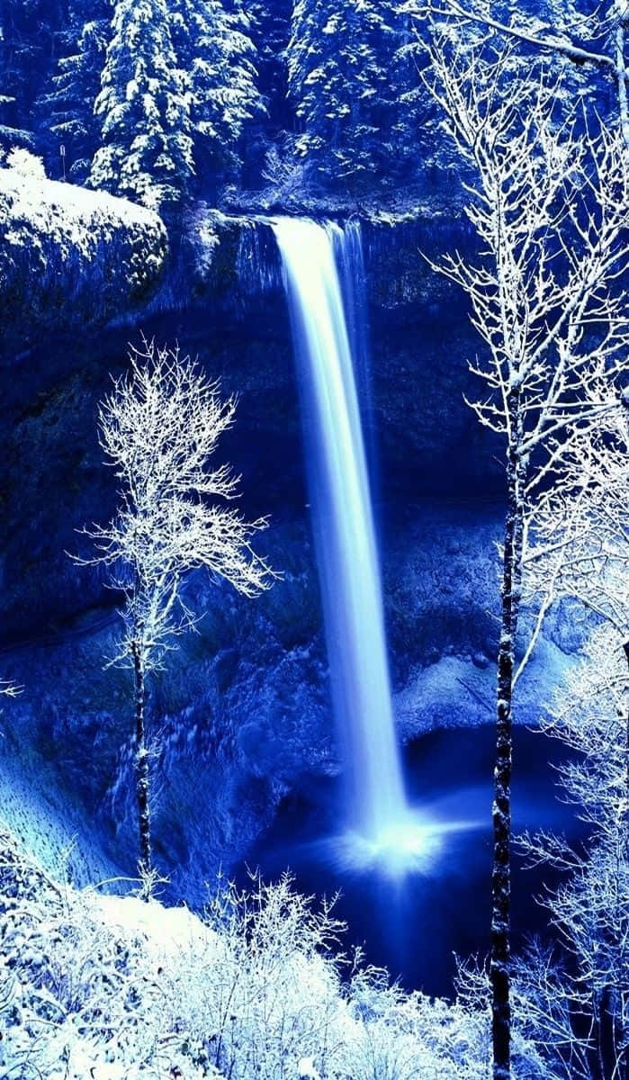 冬日森林中，被積雪覆蓋的樹木環繞著的發光藍色瀑布。