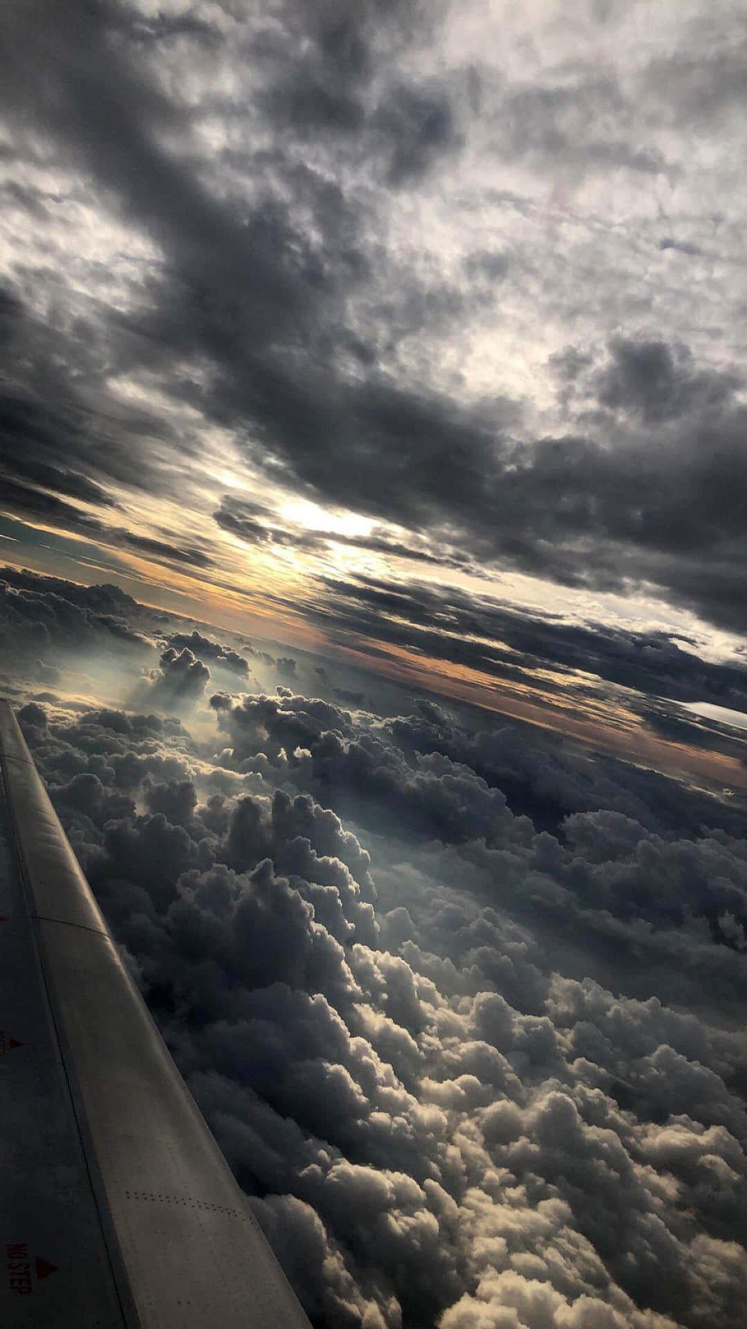 夕陽下飛機機翼在雲層之上，伴隨著戲劇性的暴風雲。