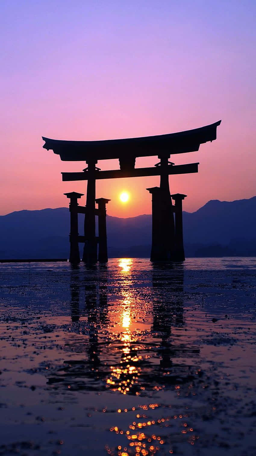 欣賞寧靜的藍色美學之美 壁紙 — 一座雄偉的鳥居在水中呈現剪影，夕陽在遠山後落下，投射出金色的倒影。