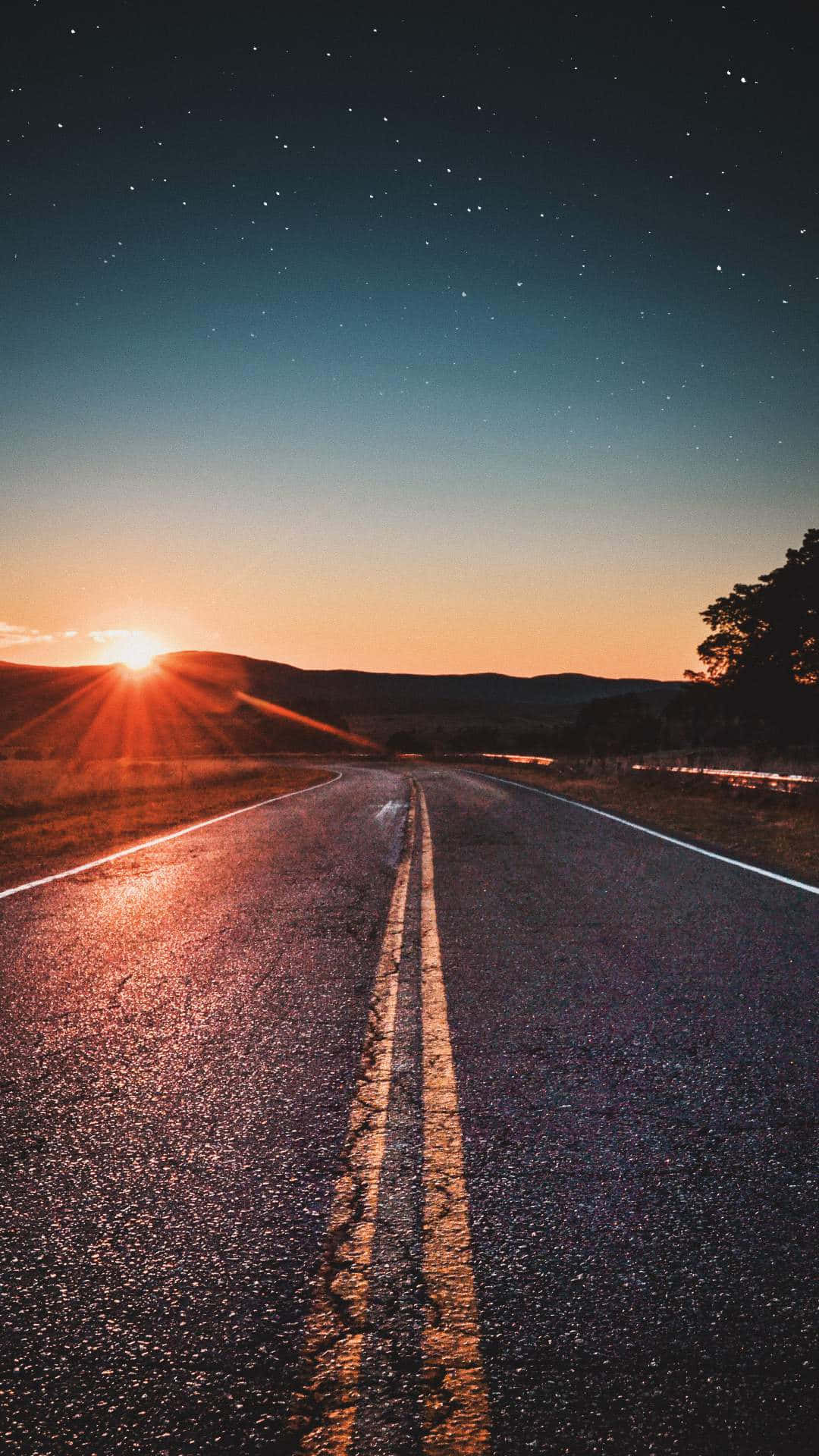 一條道路在繁星點點的暮色天空下，地平線上有發光的太陽。