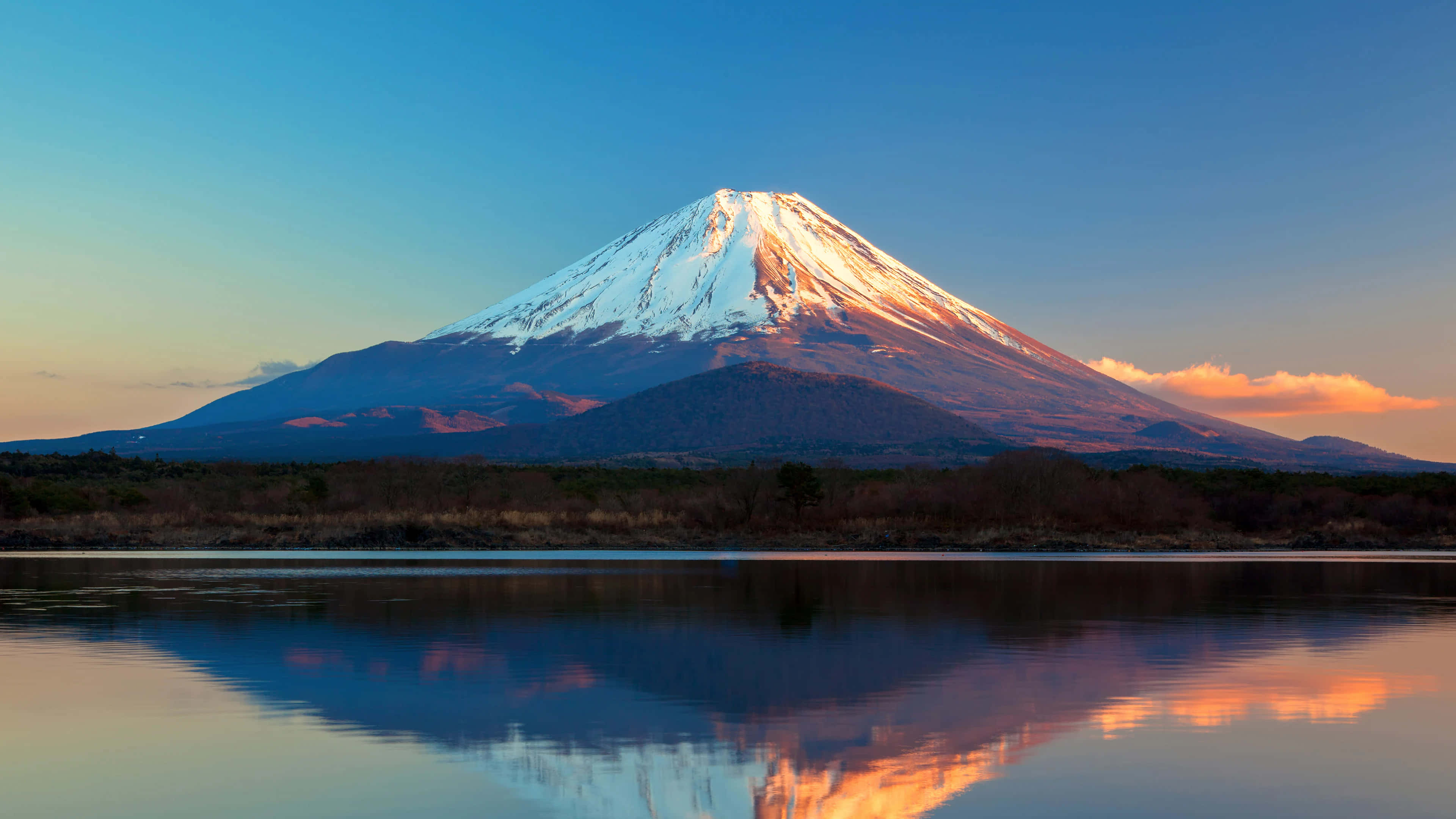 欣賞日本標誌性富士山的自然之美 壁紙 — 白雪覆蓋的富士山在日落時分完美倒映在平靜的水面上，上方有溫暖的橙色雲彩。