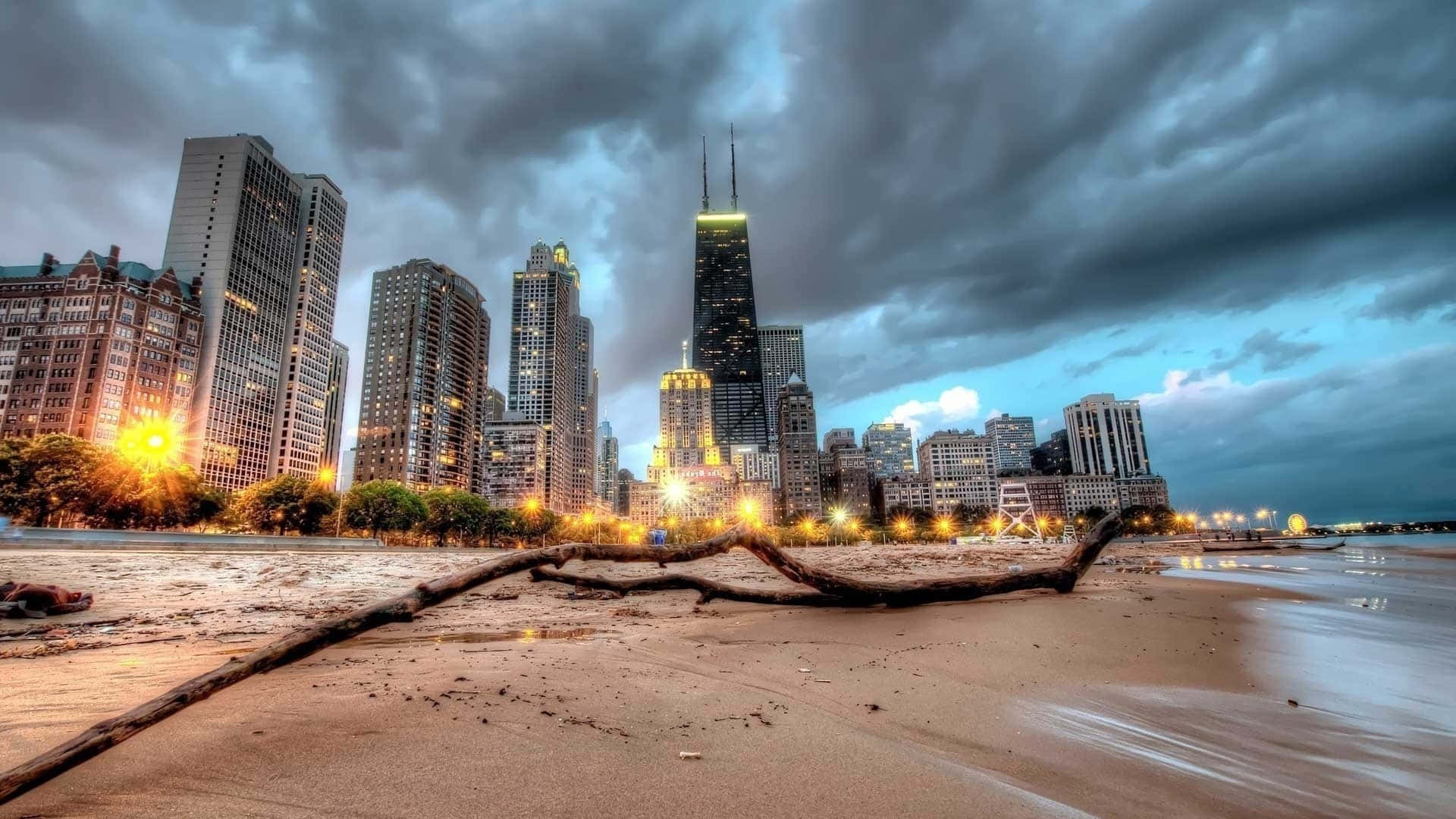 暴風雲下黃昏時分的芝加哥天際線，海灘和前景的倒下的圓木。