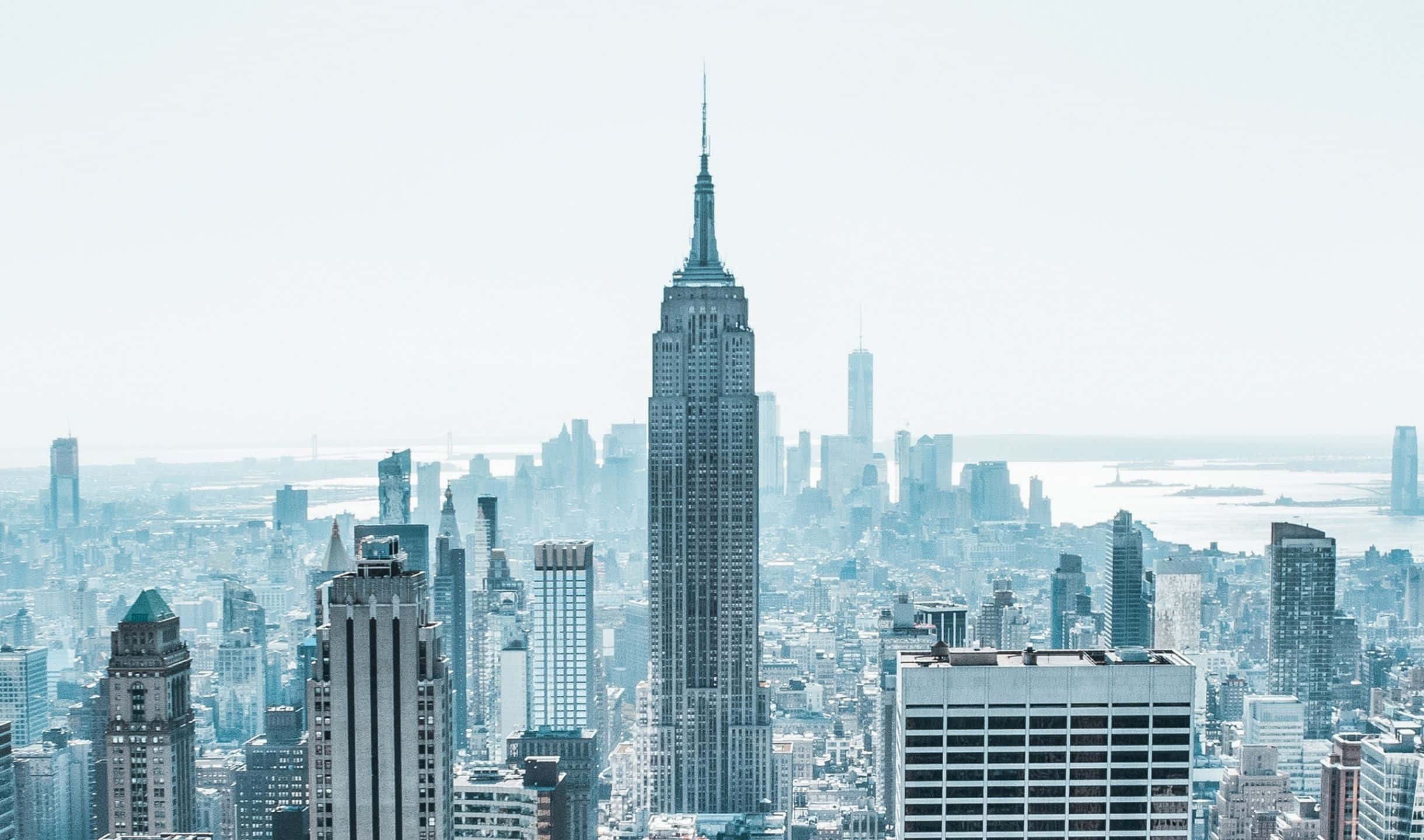 欣賞標誌性的帝國大廈的絕美風景 壁紙 — 一幅帶有朦朧藍調的紐約市天際線鳥瞰圖，以帝國大廈為主導。
