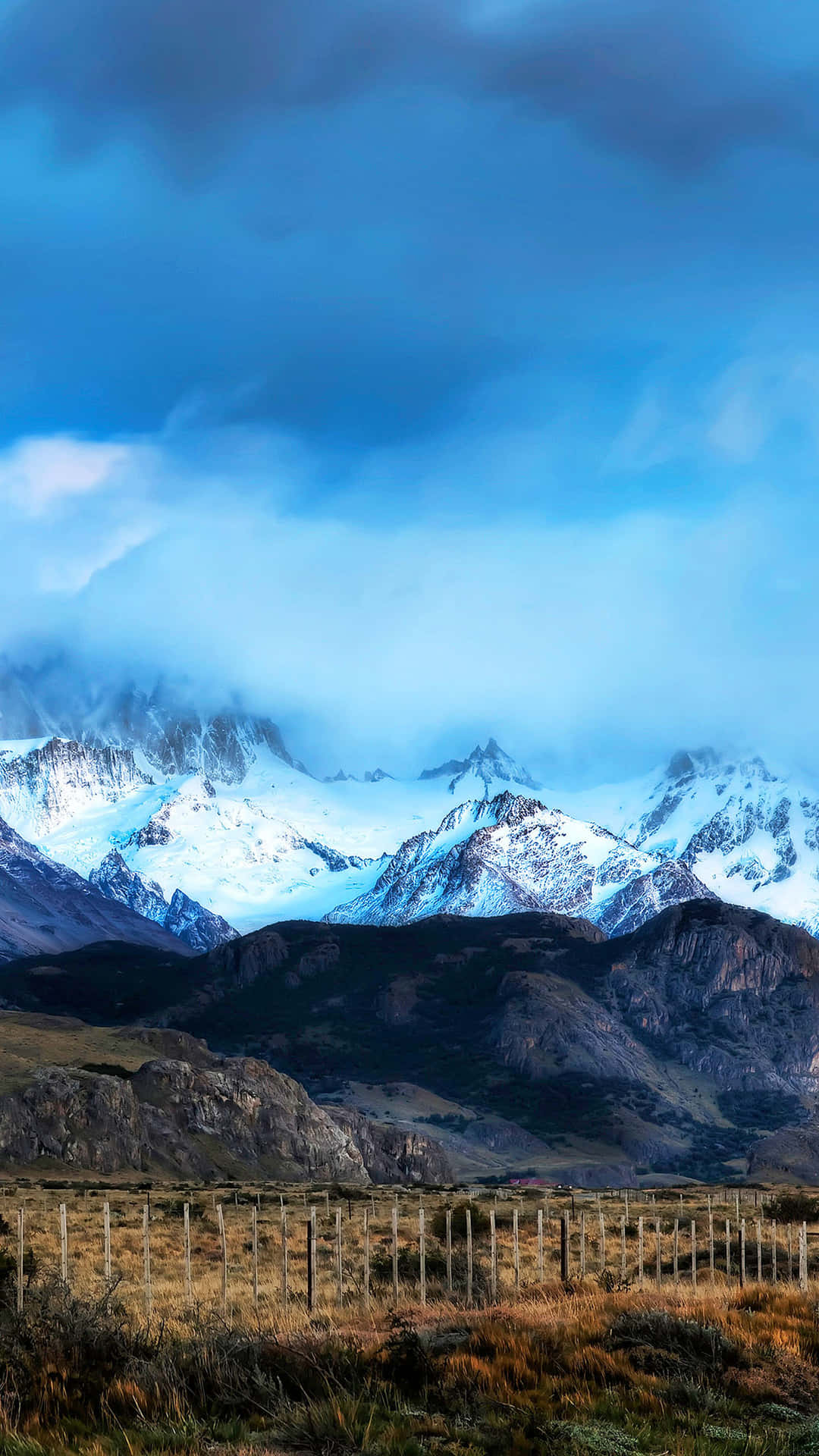 多雲天空下的雪山山脈，前景有木柵欄