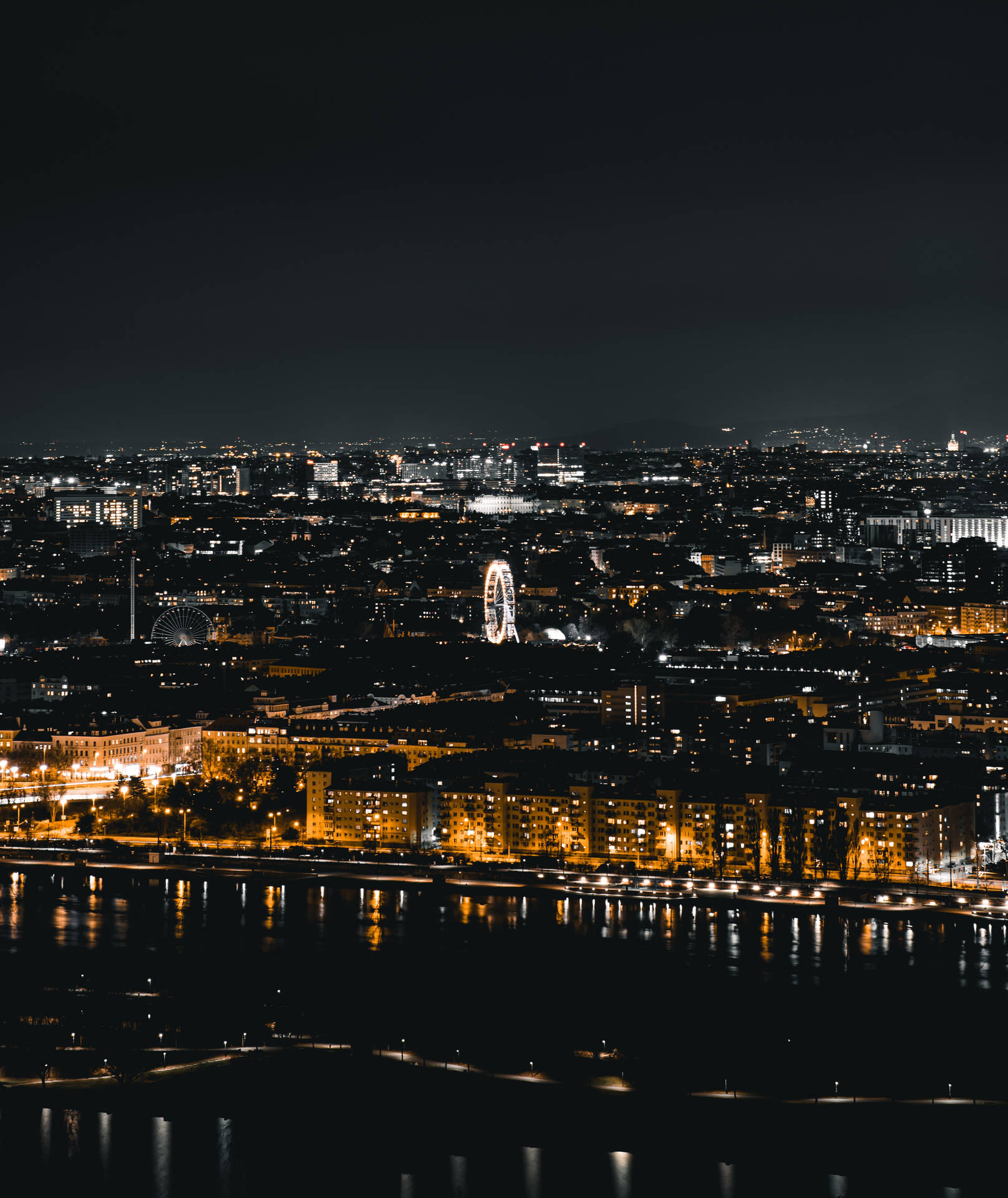 夜景城市景觀，燈光建築和摩天輪倒映在水中。
