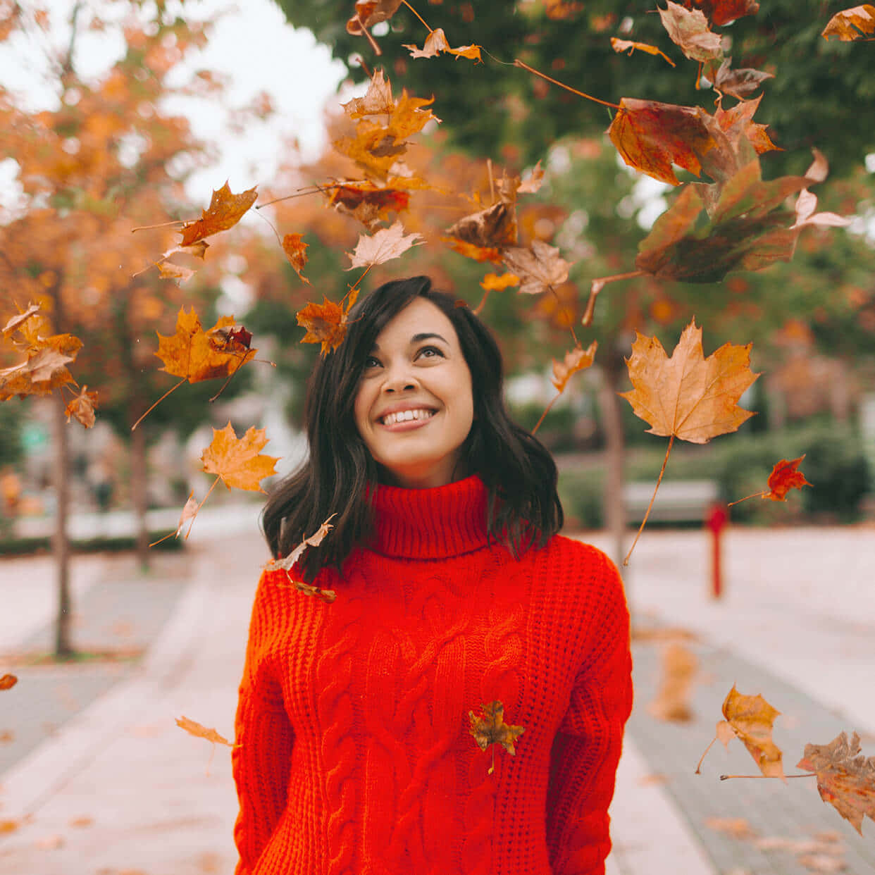 欣賞秋日的壯麗景色 🍂 壁紙 — 一位身穿紅色毛衣的快樂女性在充滿活力的秋季公園場景中微笑，秋葉在她周圍旋轉。
