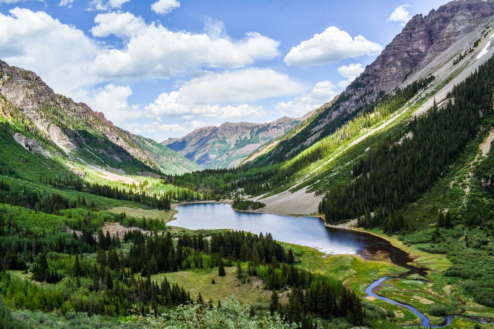 一個寧靜的山間湖泊，周圍環繞著茂密的森林和岩石山峰，天空晴朗。