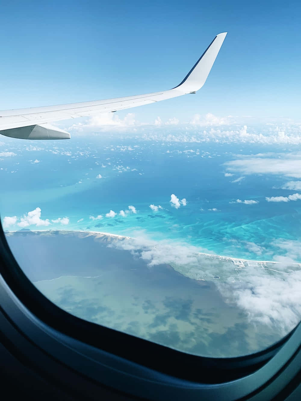 欣賞窗外景色 壁紙 — 從飛機窗戶看到的飛機機翼，俯瞰碧綠海洋和散落的雲朵，在清澈的藍天下。