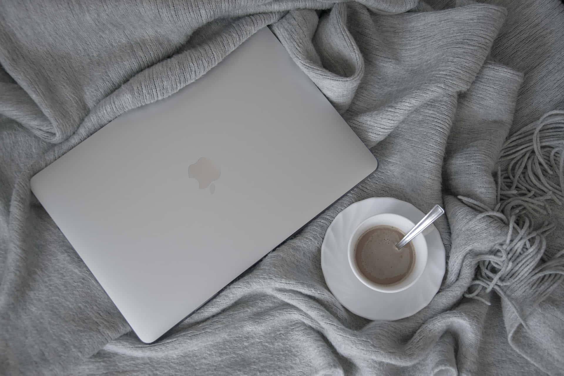 銀色手提電腦和咖啡杯在灰色毛毯上，適合舒適工作。 — 美學 MacBook 壁紙 壁紙
