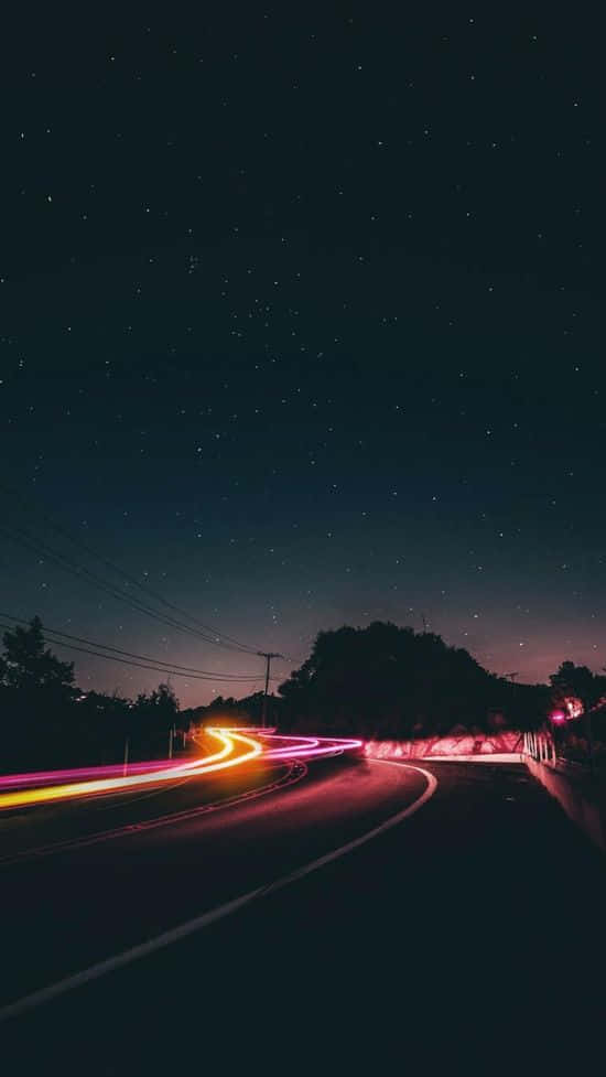 欣賞美麗的夜空 壁紙 — 夜晚星空下蜿蜒的道路，伴隨著過往車輛留下的鮮豔光軌。