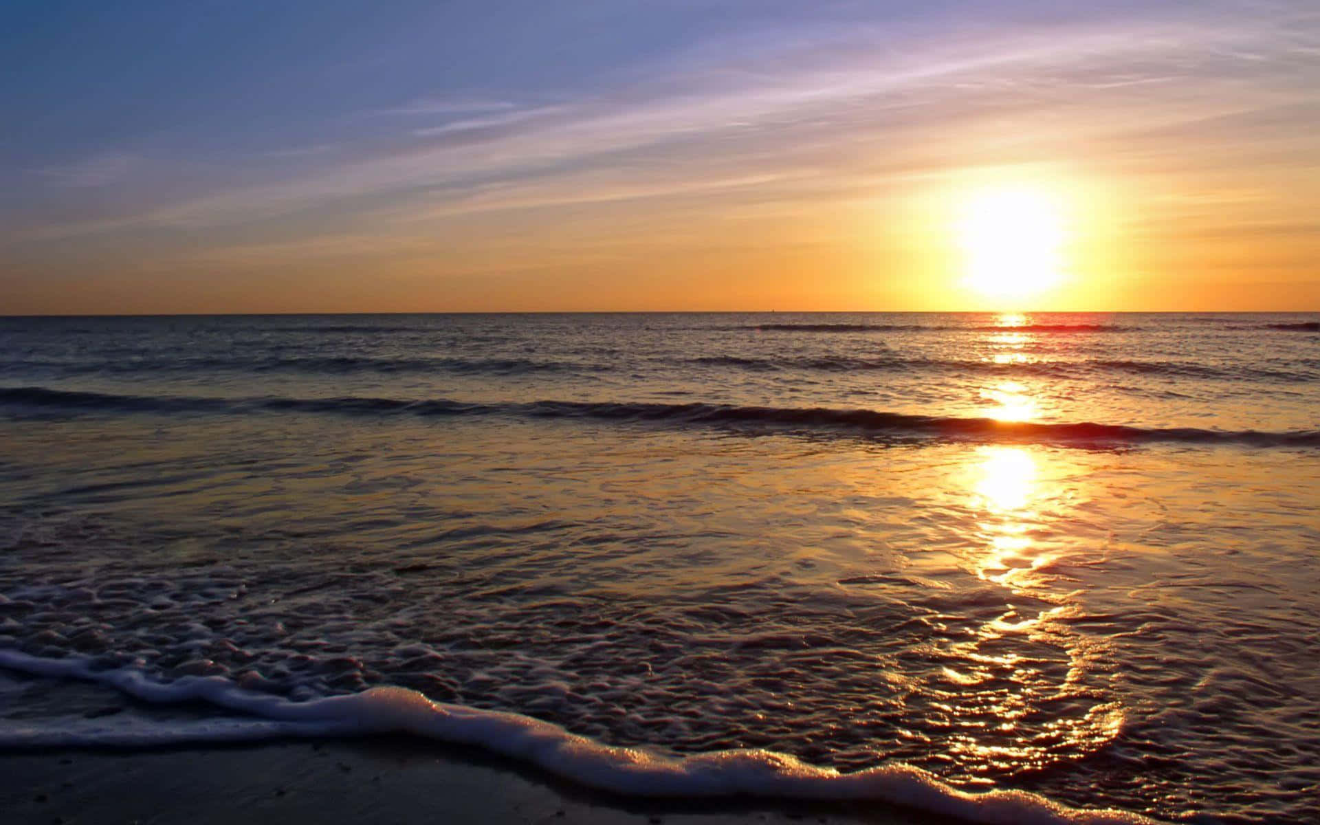 欣賞美麗的海灘日落 壁紙 — 金色夕陽照耀在平靜的海浪上，帶著柔軟的泡沫沖刷到沙灘上。