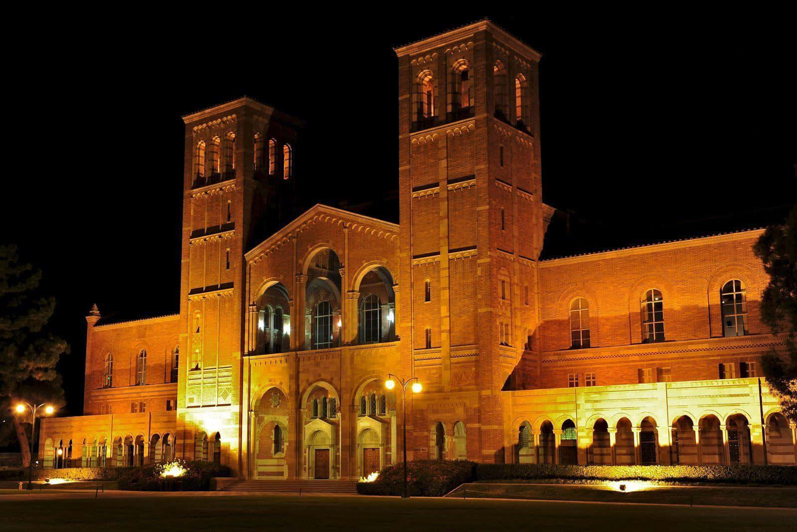 一座歷史悠久的磚造大學建築，夜晚亮起燈光，帶有拱形窗戶和塔樓。