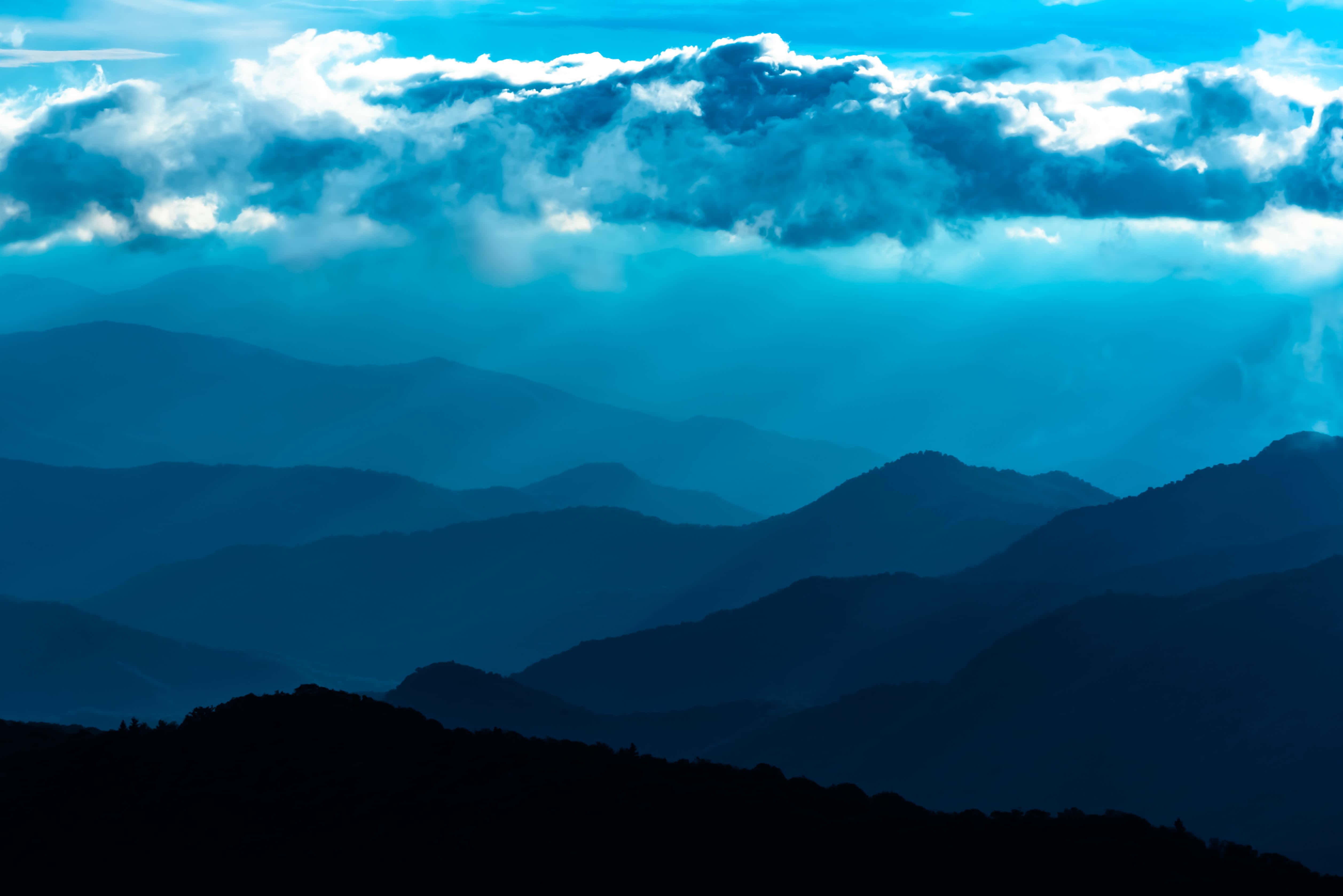 欣賞藍嶺山脈的美麗風景 壁紙 — 層層疊疊的山脈在戲劇性的多雲天空下，逐漸融入大氣藍色的薄霧中。