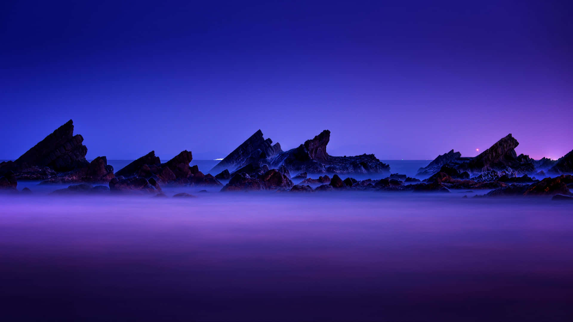 鋸齒岩石從霧氣瀰漫的水中浮現，背景是紫色暮色天空。