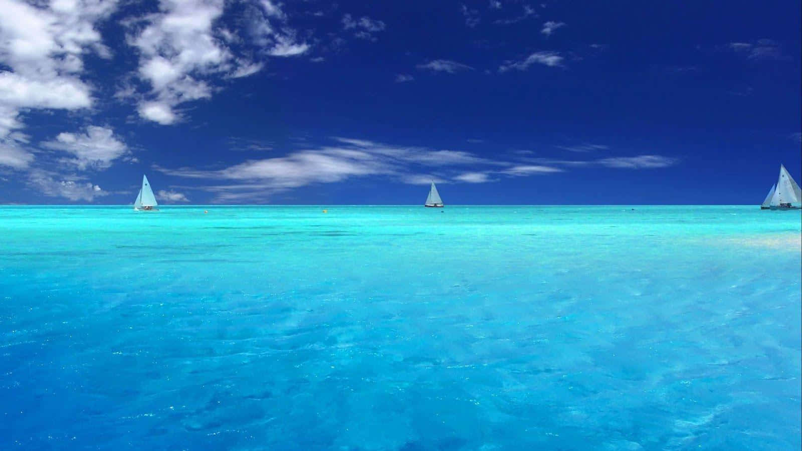 三艘帆船漂浮在碧綠的海水上，天空湛藍，白雲朵朵。