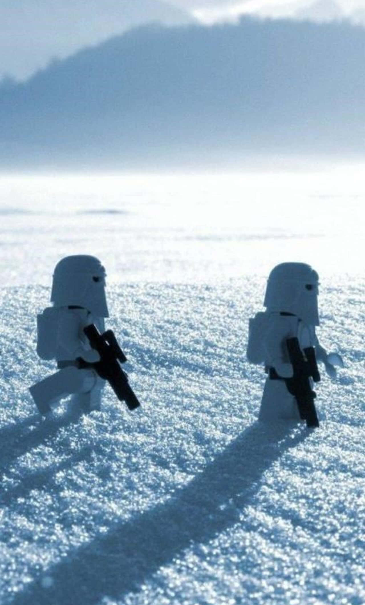 欣賞這些可愛青綠色iPhone的色彩與風格 壁紙 — 兩個 LEGO 雪地兵團在一片廣闊的雪原上行進，背景是朦朧的藍天和遠山。