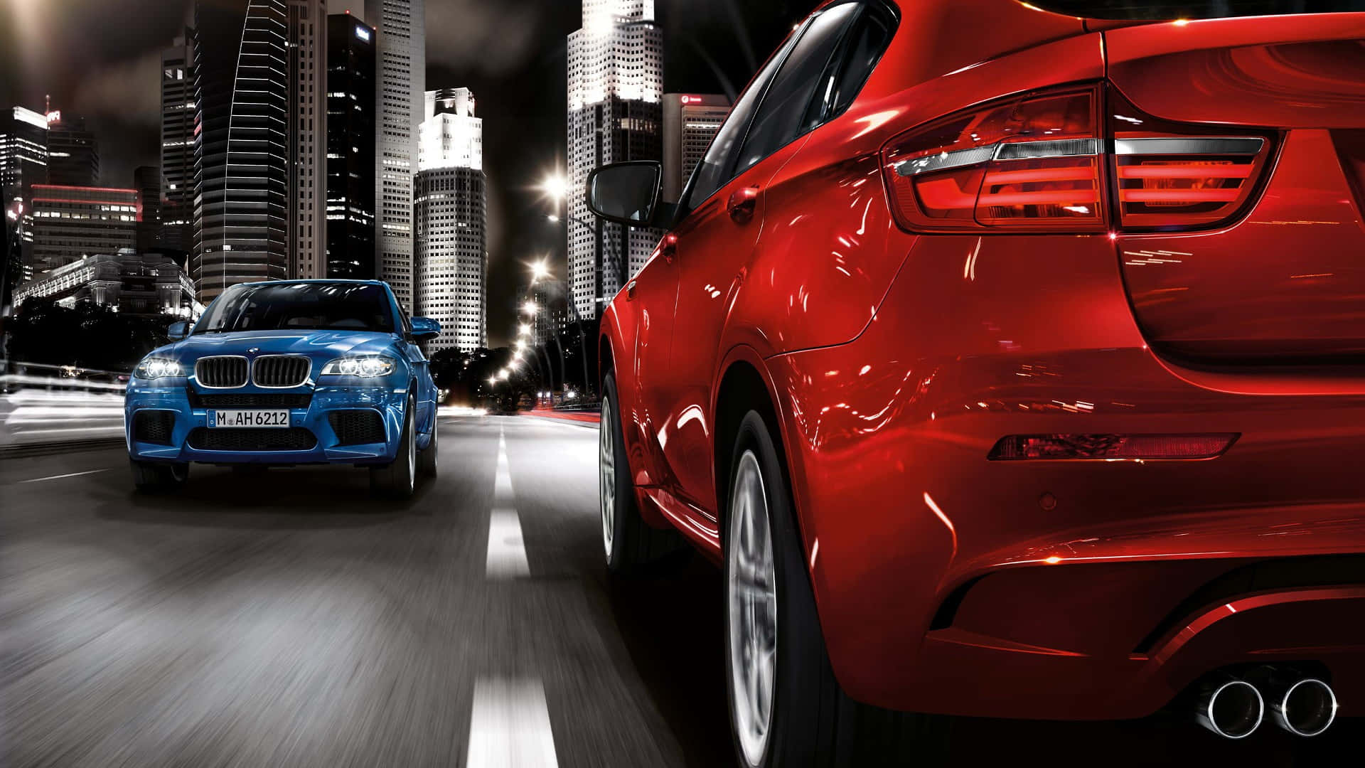 欣賞這款強勁的 BMW X6 M 壁紙 — 兩輛時尚跑車在霓虹燈閃爍的夜晚城市中飛馳，背後是高聳入雲的摩天大樓閃閃發光。