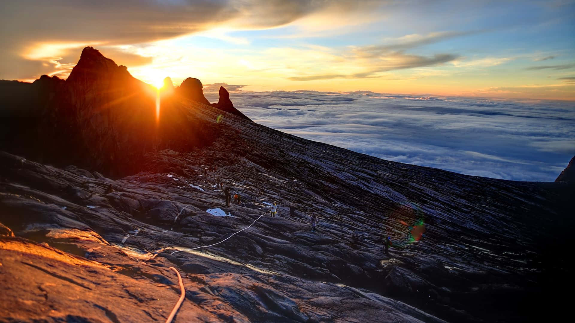 登山者在日出時攀登雲海之上的岩石山峰。