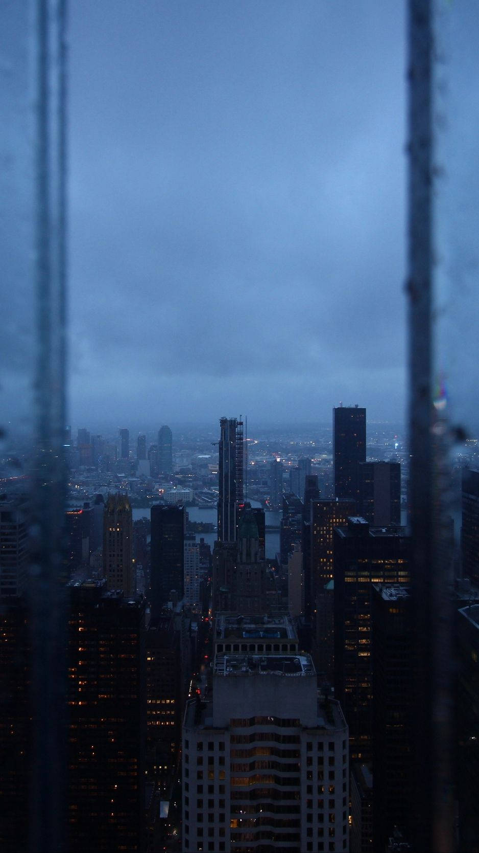 從雨濕的窗戶觀看黃昏時分的城市天際線，閃爍的燈光。