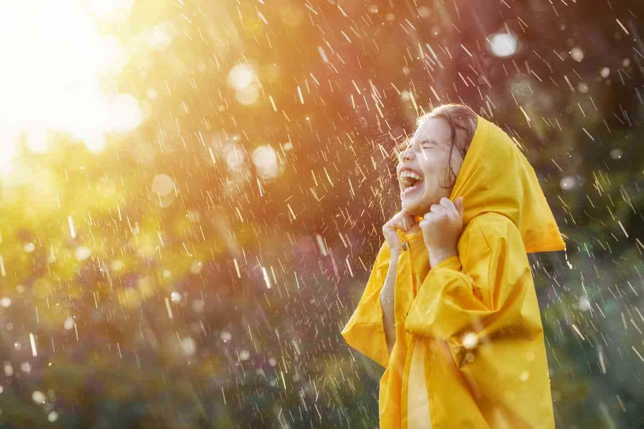 穿著黃色雨衣的孩子在雨中大笑，背後有陽光。