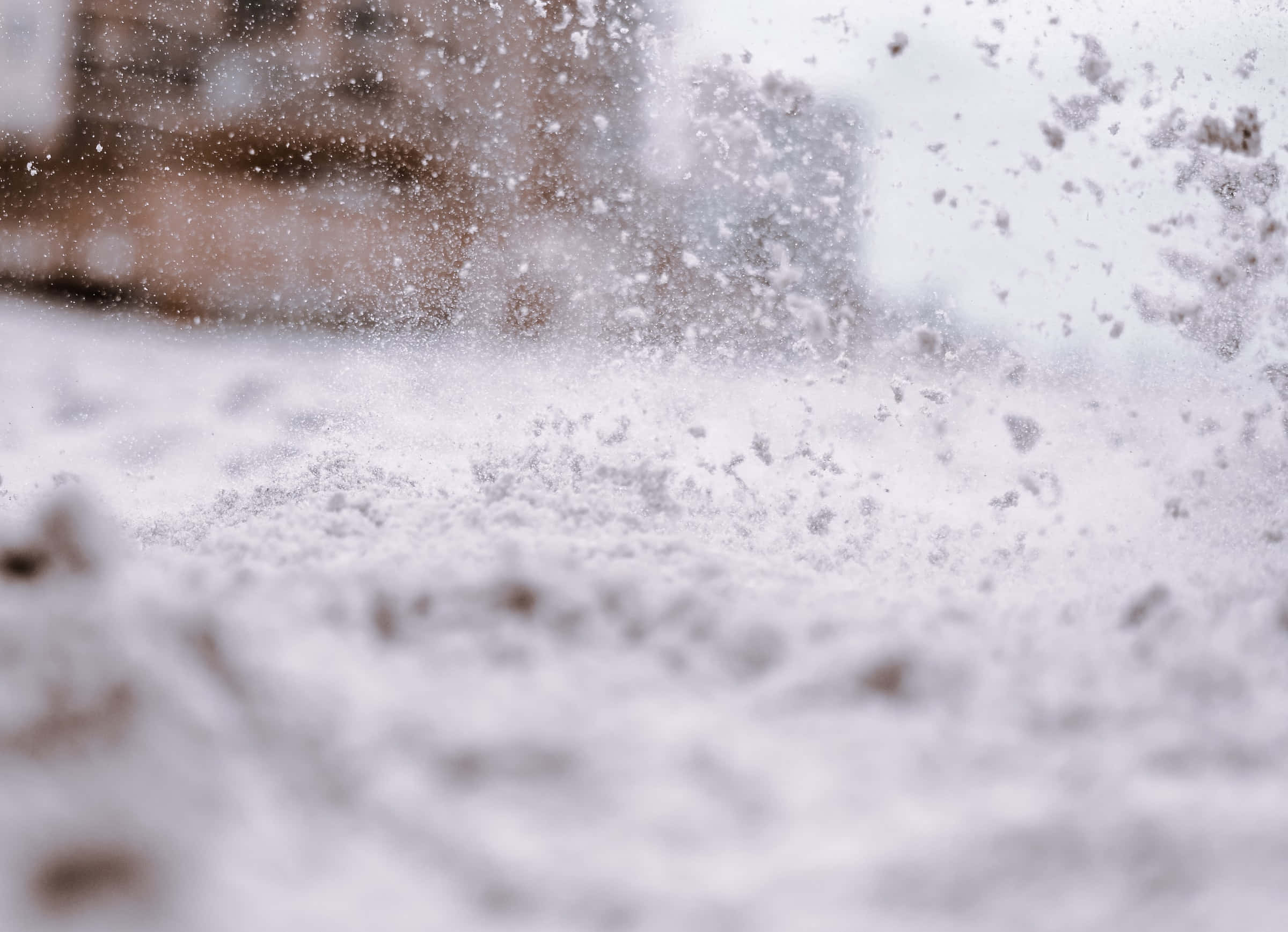 欣賞雪景的美麗風光 壁紙 — 雪花在半空中懸浮的特寫，背景是模糊的城市景觀，帶有柔和的白色和灰色色調。