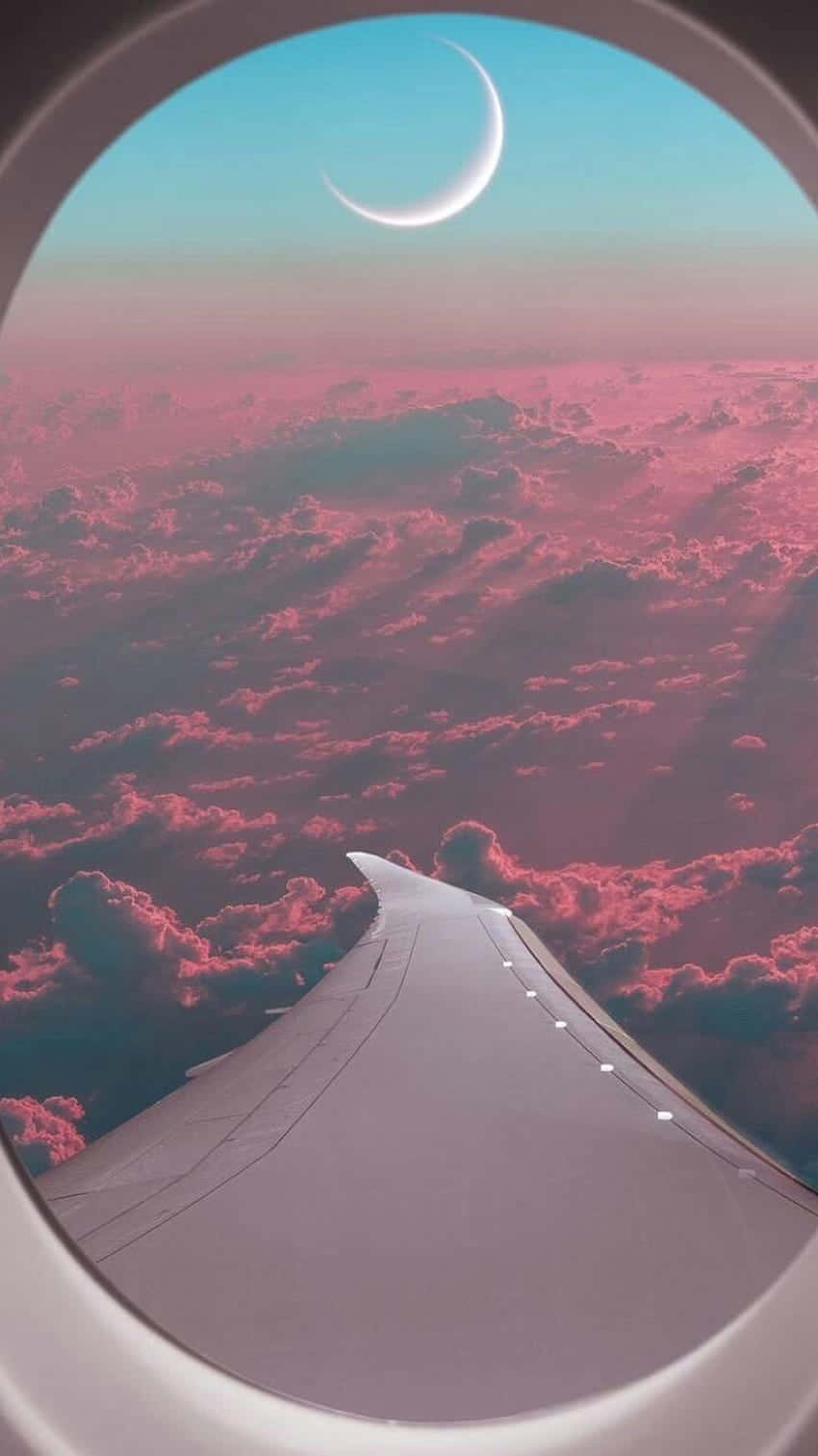 欣賞飛機窗戶的風景 壁紙 — 透過飛機窗戶看到的機翼，背景是暮色天空中的粉紅雲朵和彎月。