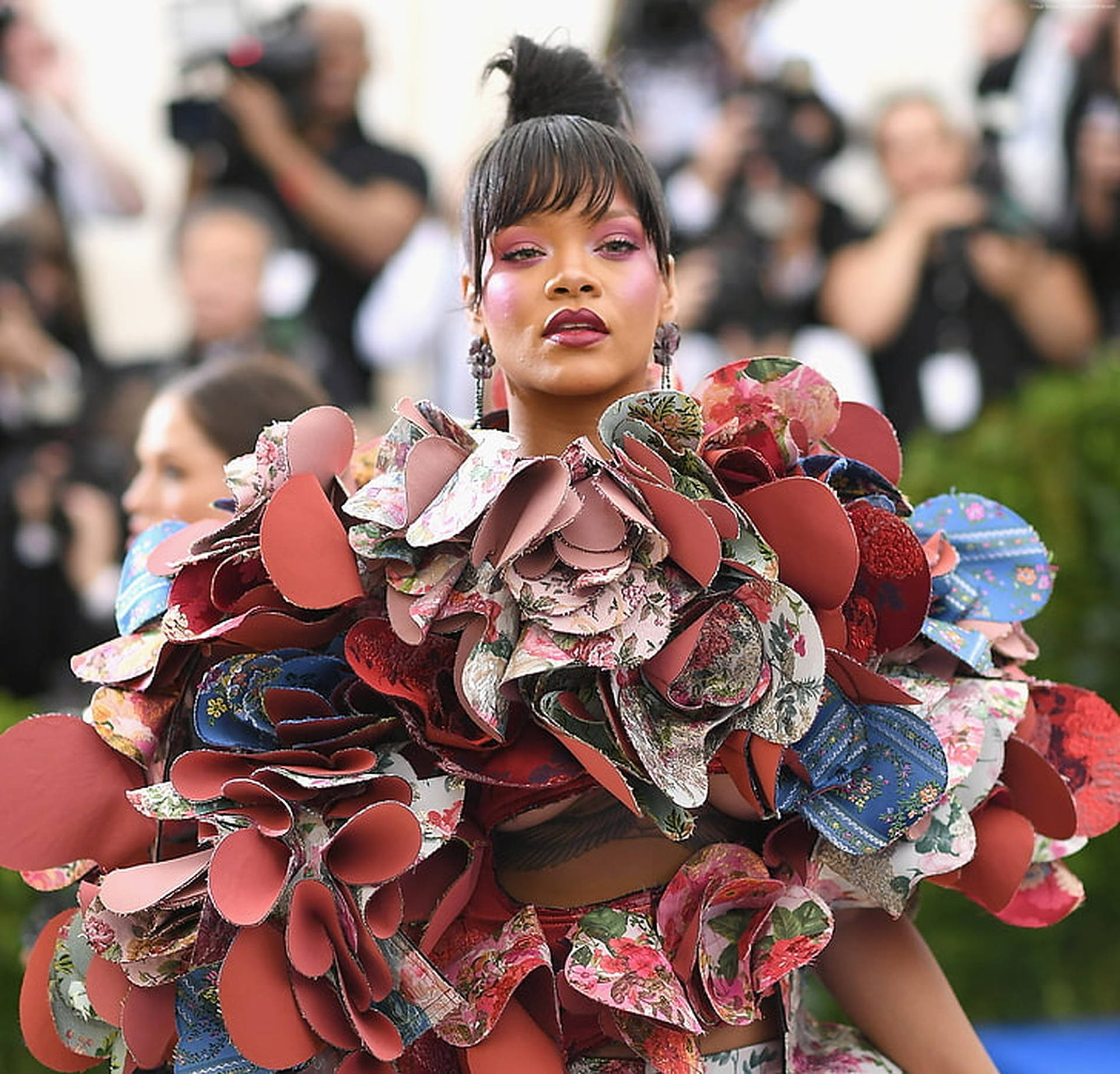 Rihanna 喺紅地毯活動中穿著一件花卉圖案長袍，上面有層疊嘅布料花瓣。