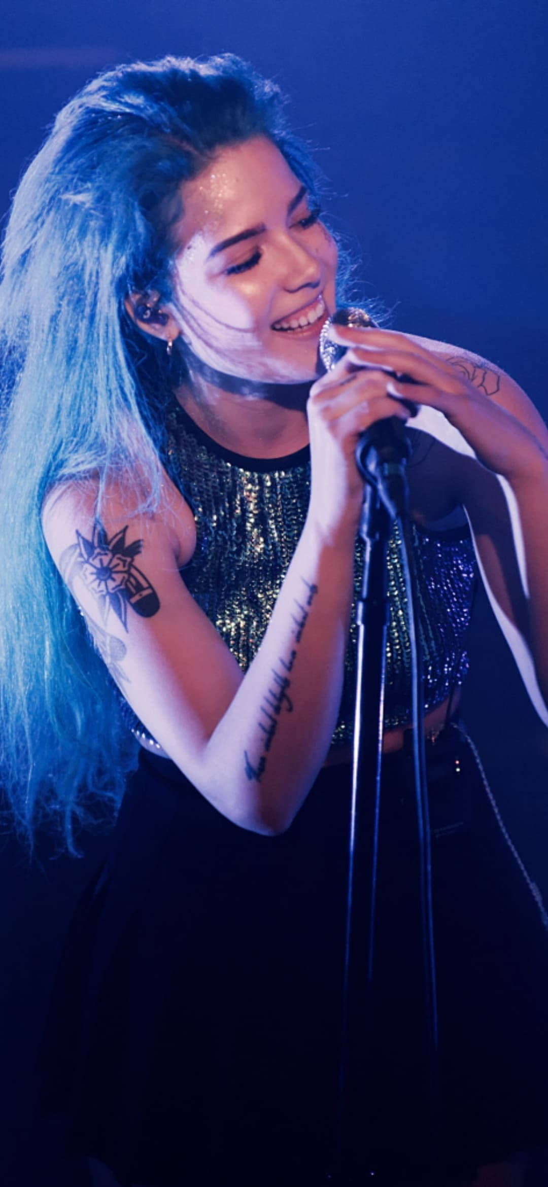 歌手Halsey舞台演出 壁紙 — 一位藍髮、有紋身的女歌手在藍色舞台燈光下熱情地對著麥克風演唱。