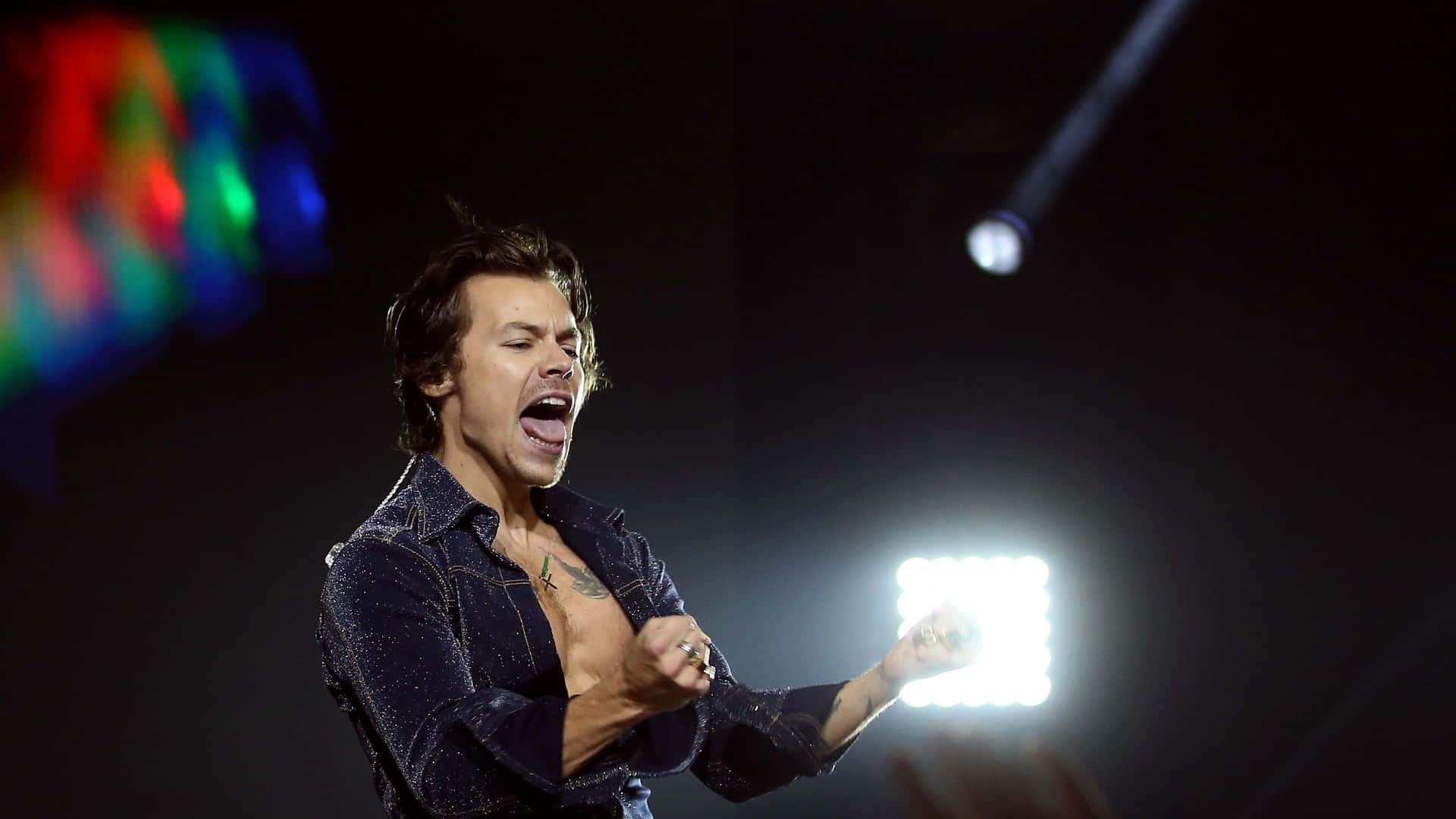 Harry Styles 在明亮的燈光下，在音樂會舞台上熱情歌唱。