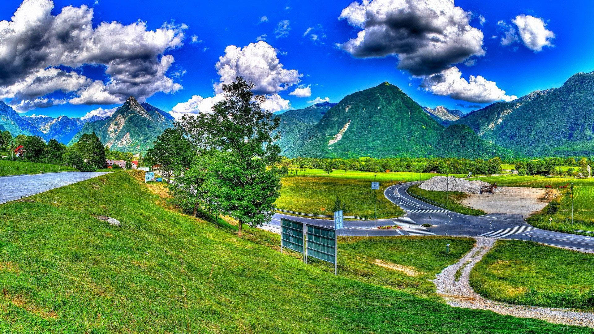 蜿蜒的道路穿過綠色田野，背景有山脈和雲彩