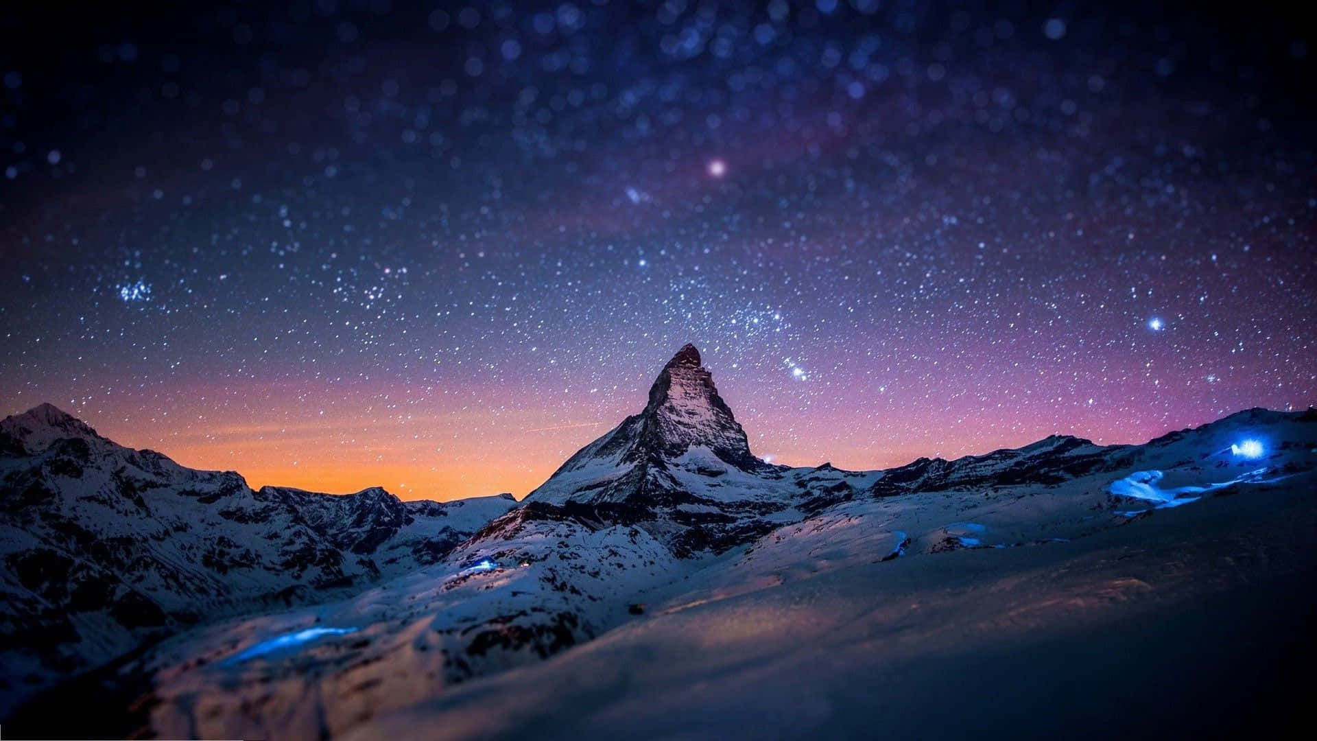 歐洲阿爾卑斯山最佳電腦背景 壁紙 — 白雪覆蓋的馬特洪峰在星空暮色下聳立，天空呈現紫橙色漸變，雪坡上閃爍著藍色光芒。