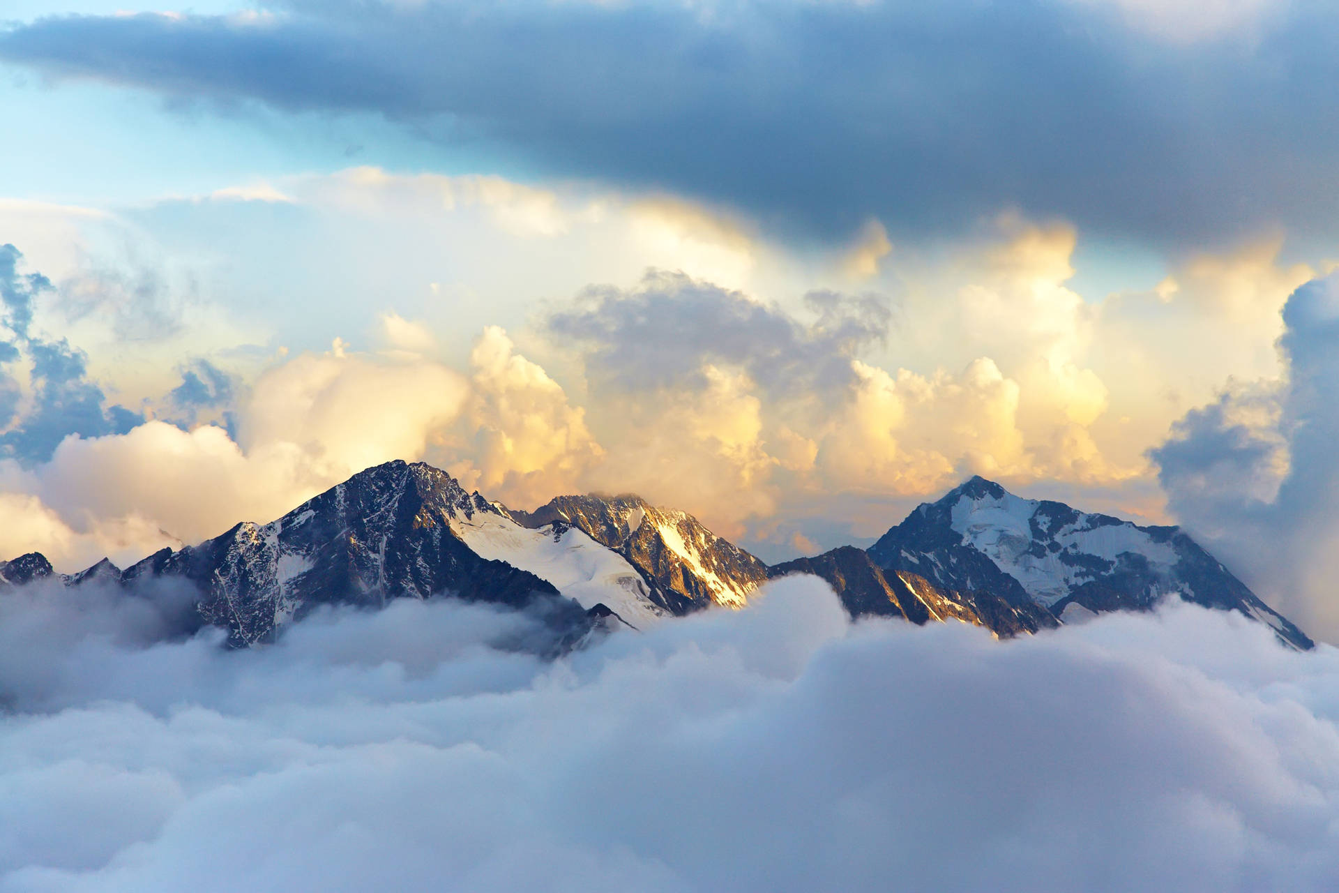日出時，積雪的山峰聳立於雲層之上。 — 雲朵 壁紙