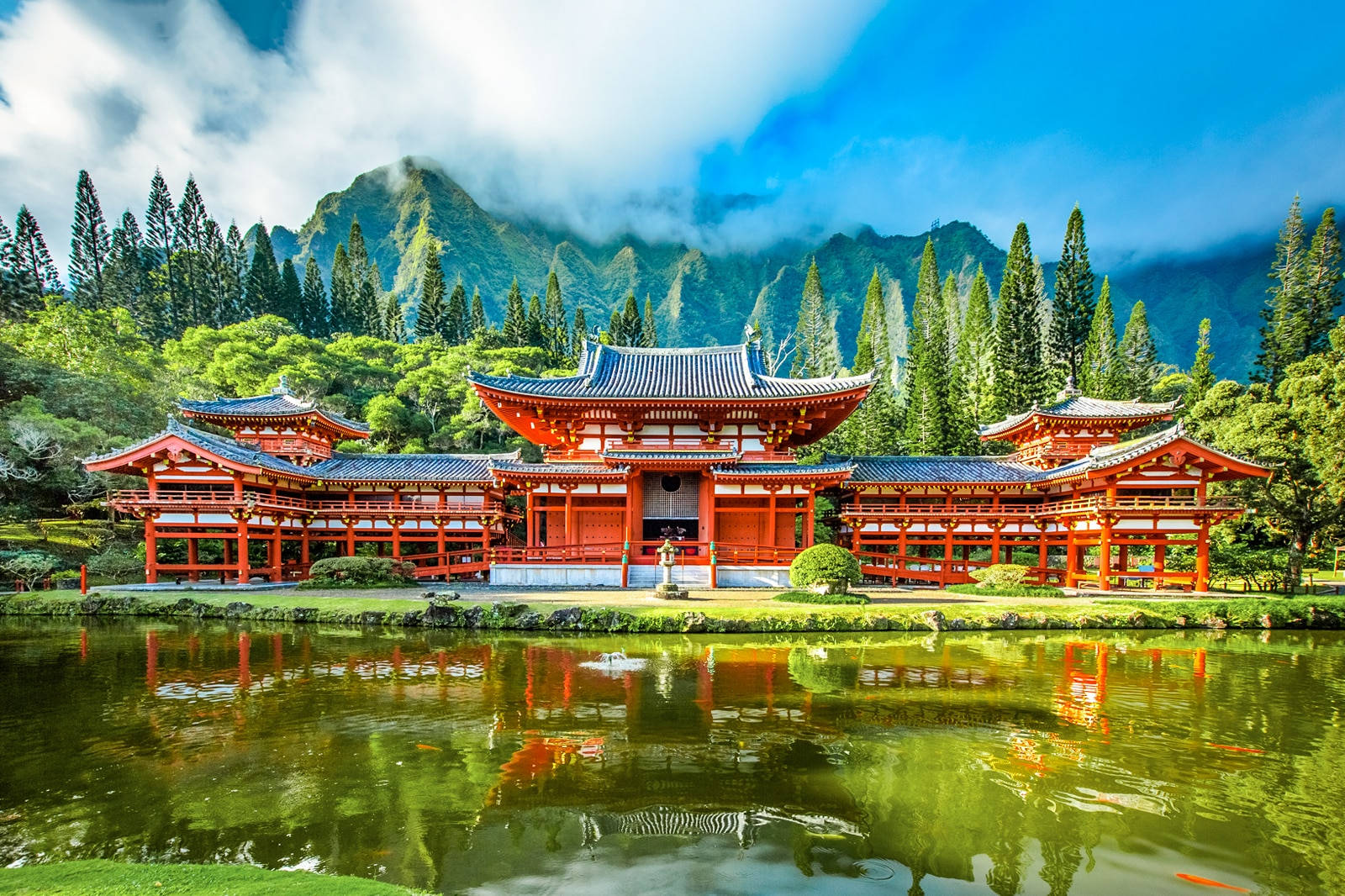 歐胡島比叡寺 壁紙 — 一座鮮紅色的日本寺廟，帶有藍色瓦片屋頂，倒映在平靜的池塘中，周圍環繞著茂密的綠樹和霧氣繚繞的山脈，天空湛藍明亮。