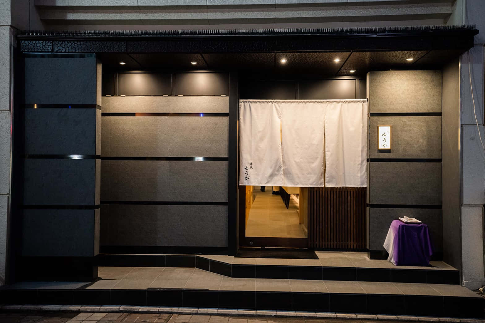 夜晚日本餐廳入口，發光暖簾和紫色桌布。