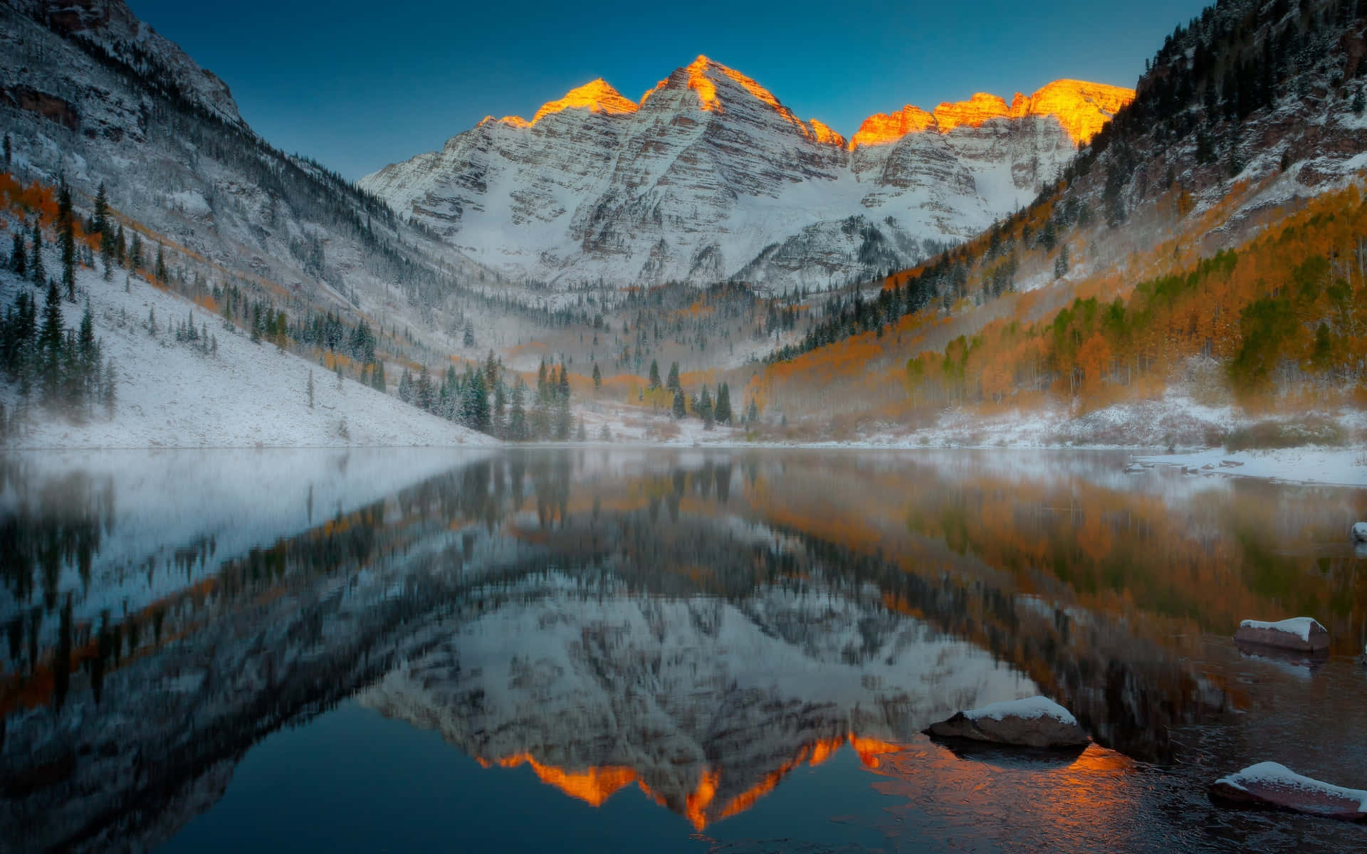 積雪的山峰在日出時閃耀，倒映在霧氣湖中，伴隨著秋樹。