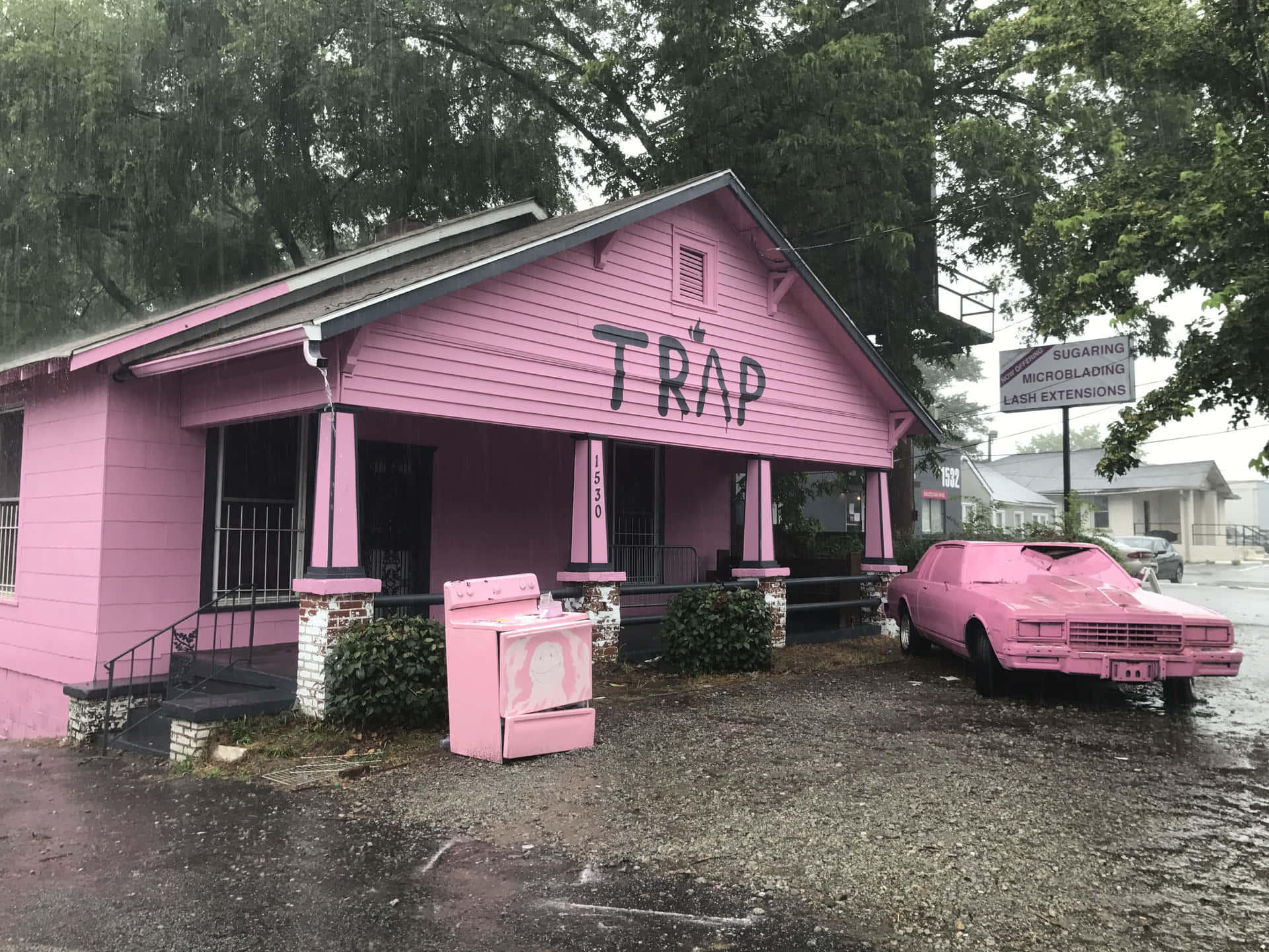 雨中的粉紅色建築物和汽車，側面有'TRAP'塗鴉。