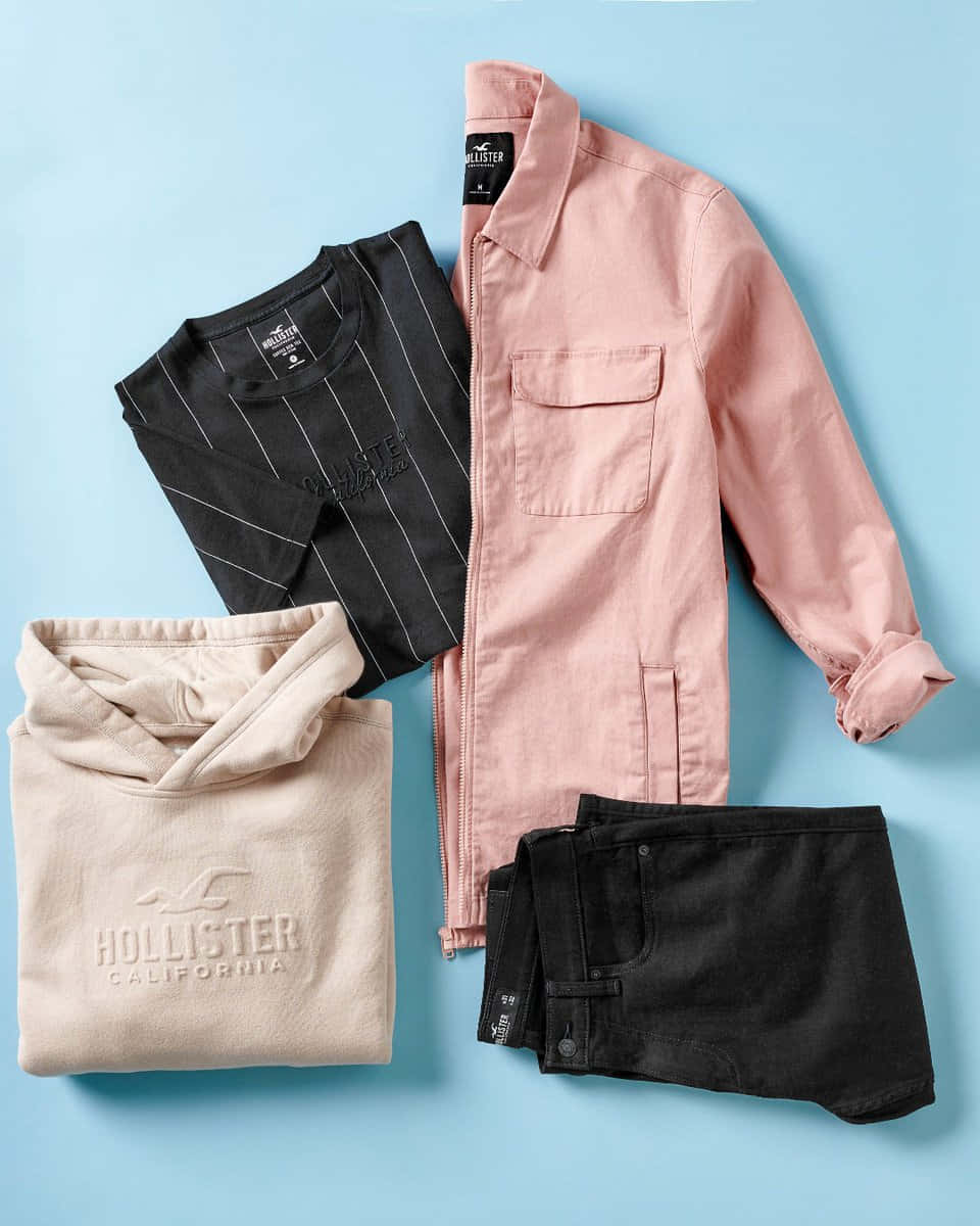 折疊的 Hollister 服裝套裝，包括外套、T 恤、連帽衫和短褲，背景為藍色。