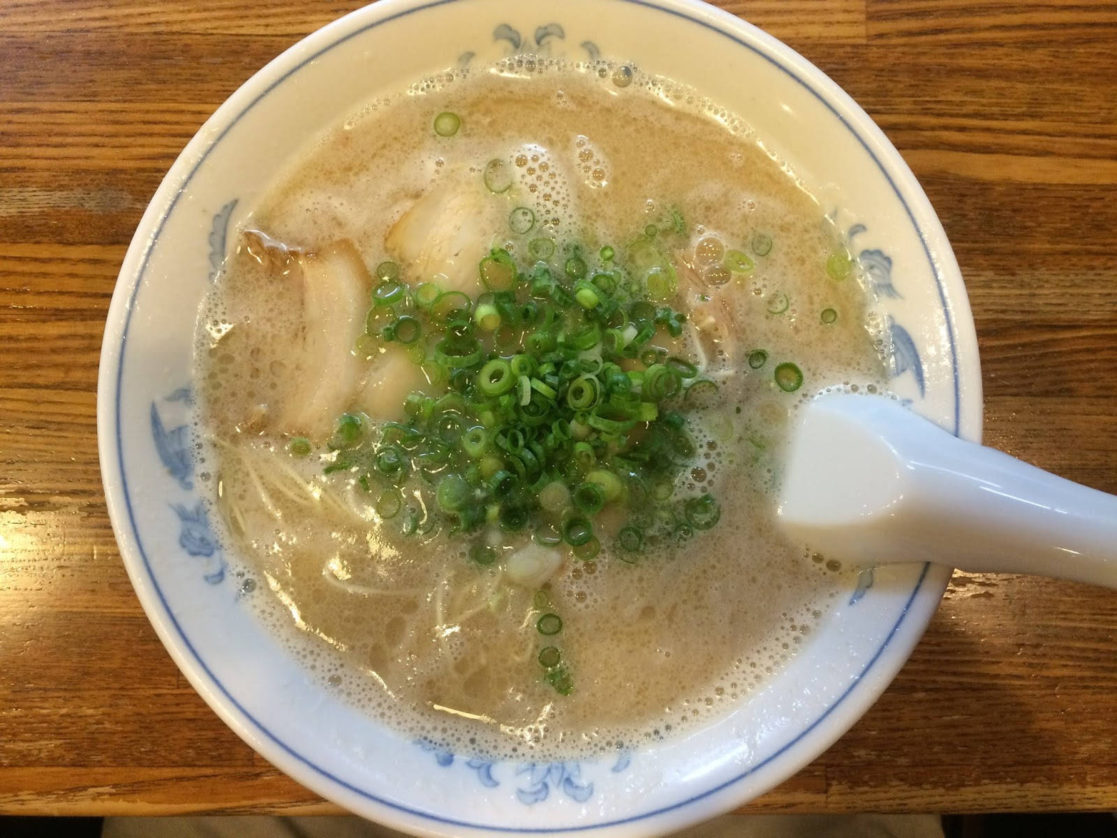 一碗拉麵配青蔥和湯匙，放在木桌上。
