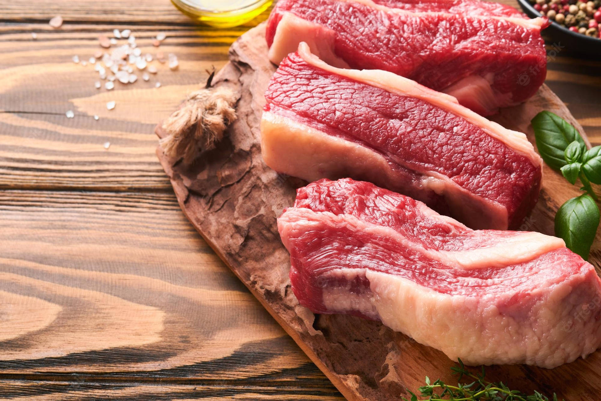 木砧板上嘅三塊生牛肉扒，配有鹽、油同香草。