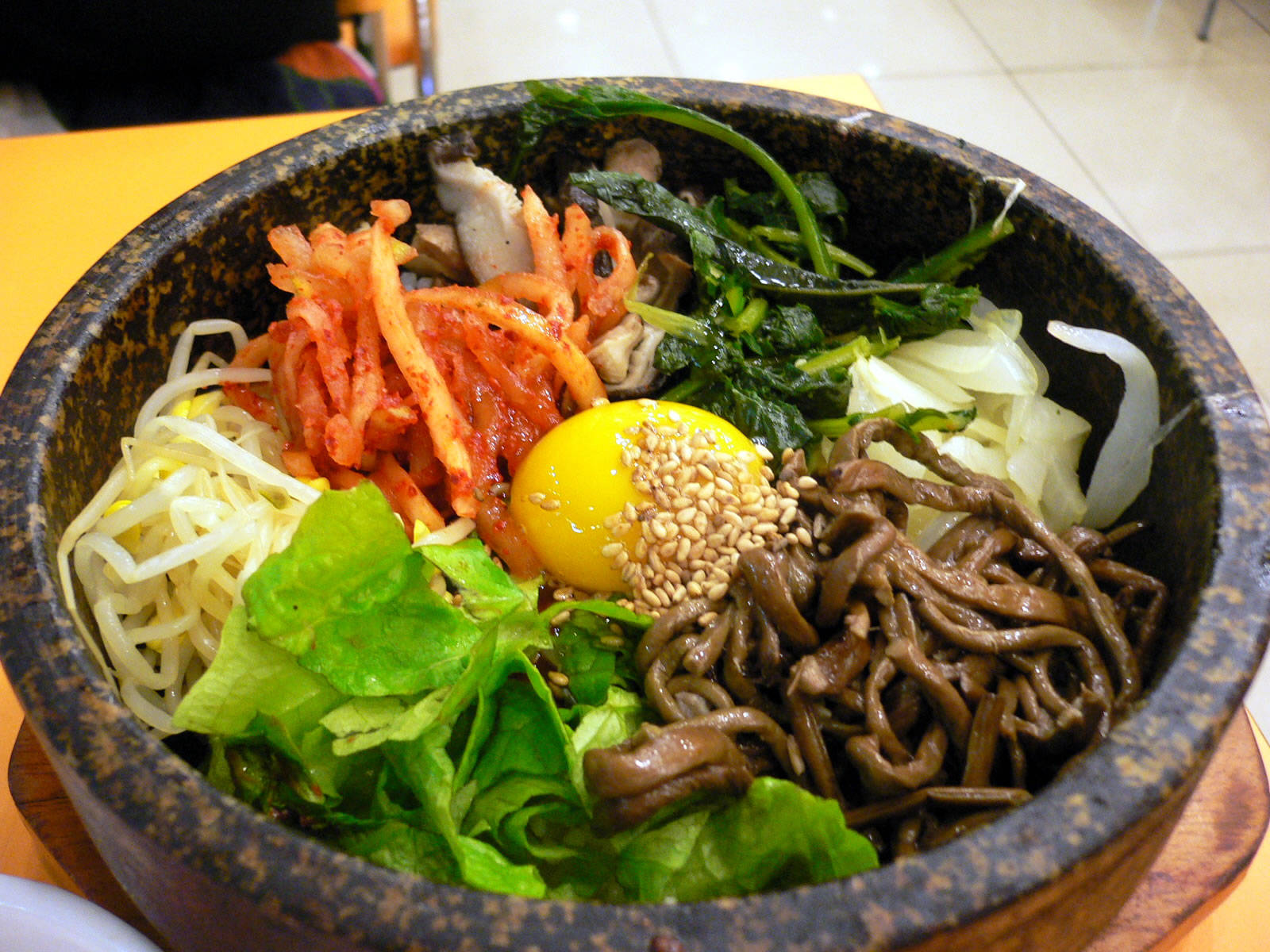 正宗韓式拌飯碗 壁紙 — 一個冒煙的石鍋韓國拌飯，上面放著鮮豔的泡菜、生雞蛋、芝麻和新鮮蔬菜。