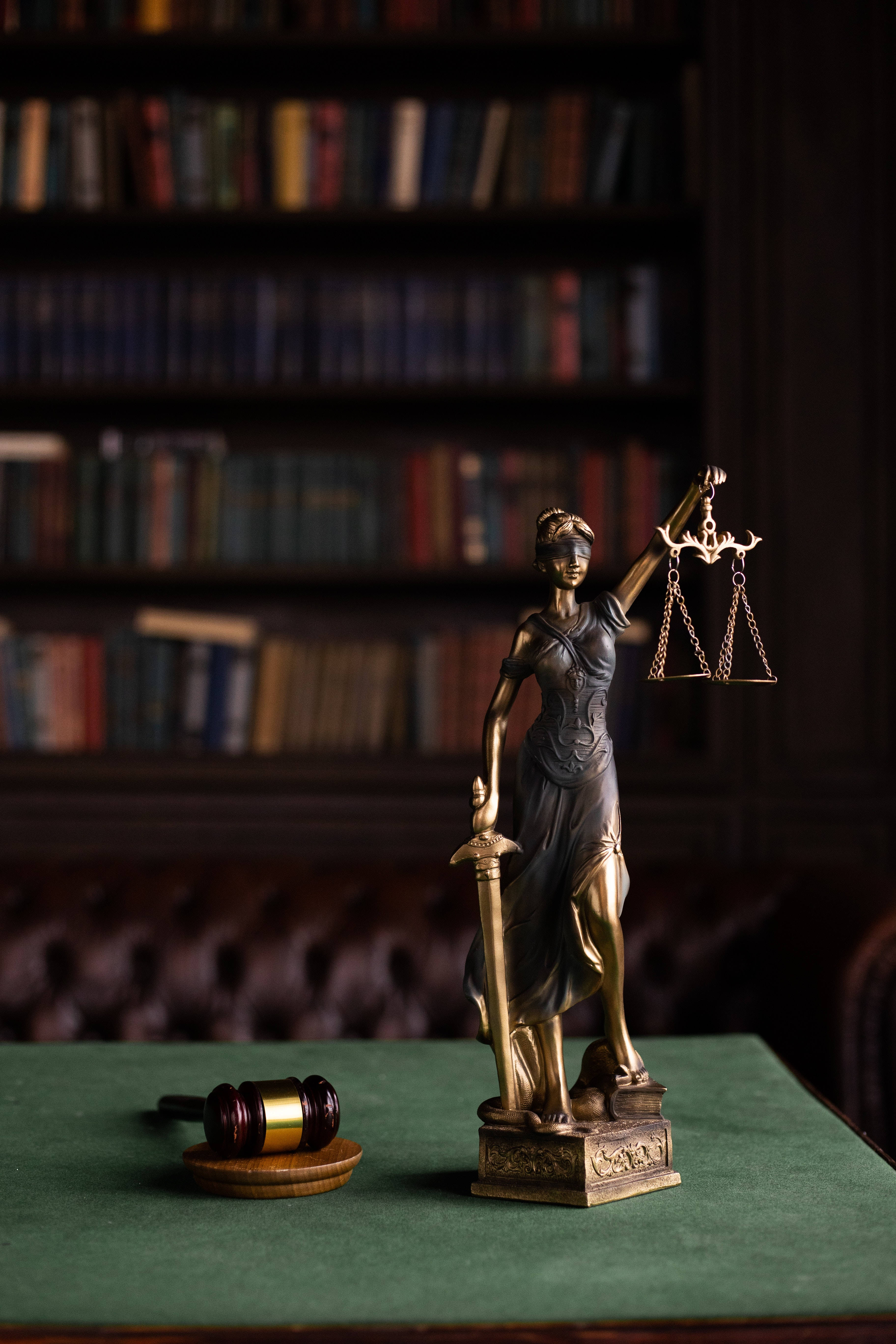 Lawyer 桌布 壁紙 — 正義女神青銅像手持天秤和劍，站在綠色布上，旁邊有木槌，前方是書架。