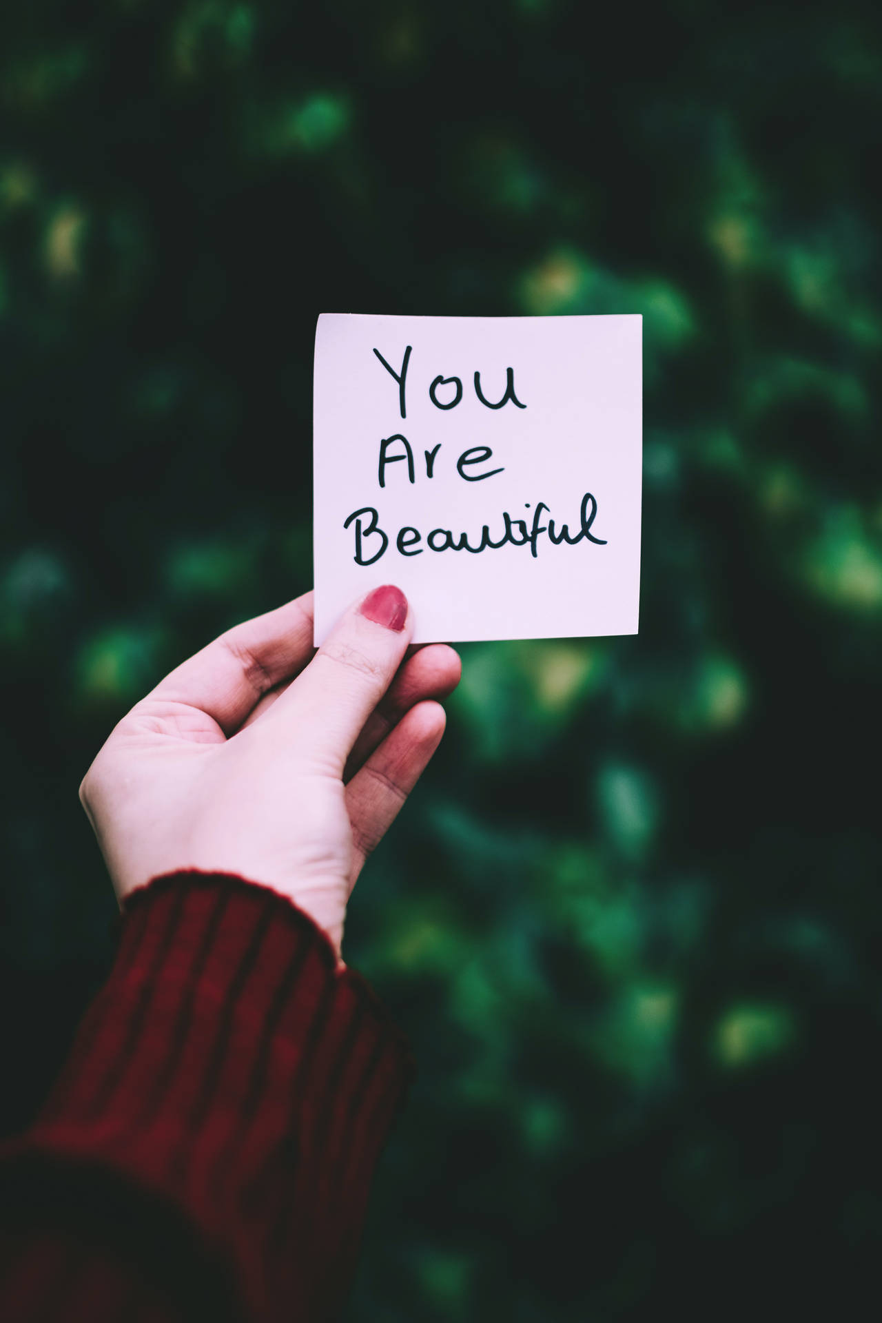 手拿著寫有 You Are Beautiful 的便條，背景為綠色