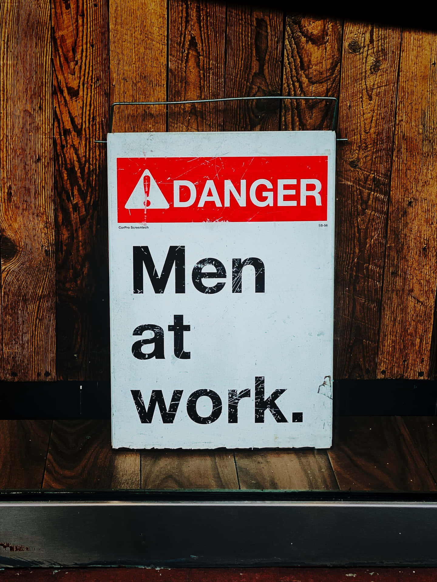 一塊磨損的警告標誌，上面寫著「Men at work」，安裝在木牆上。
