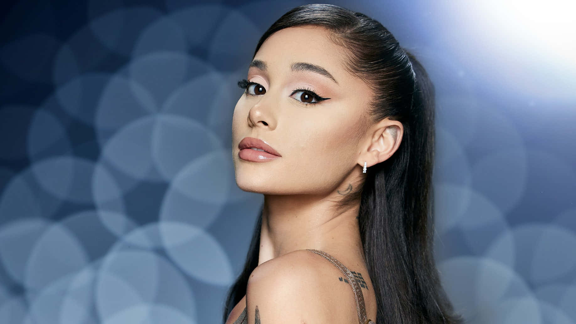 歷久彌新的美麗 壁紙 — Ariana Grande 以大膽眼線在柔和藍色散景背景前自信地凝視。