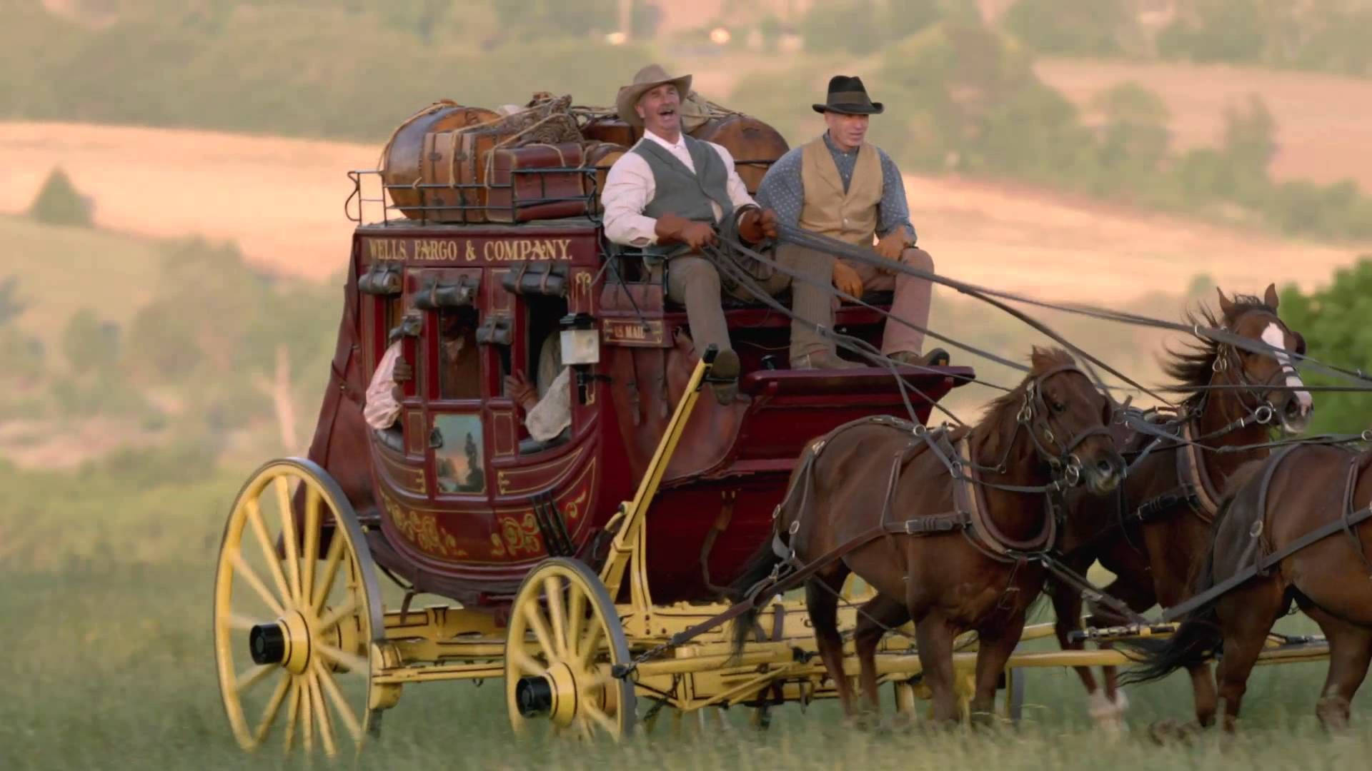 一輛紅色的 Wells Fargo 驛馬車，有兩名男子和兩匹馬在草地上移動。