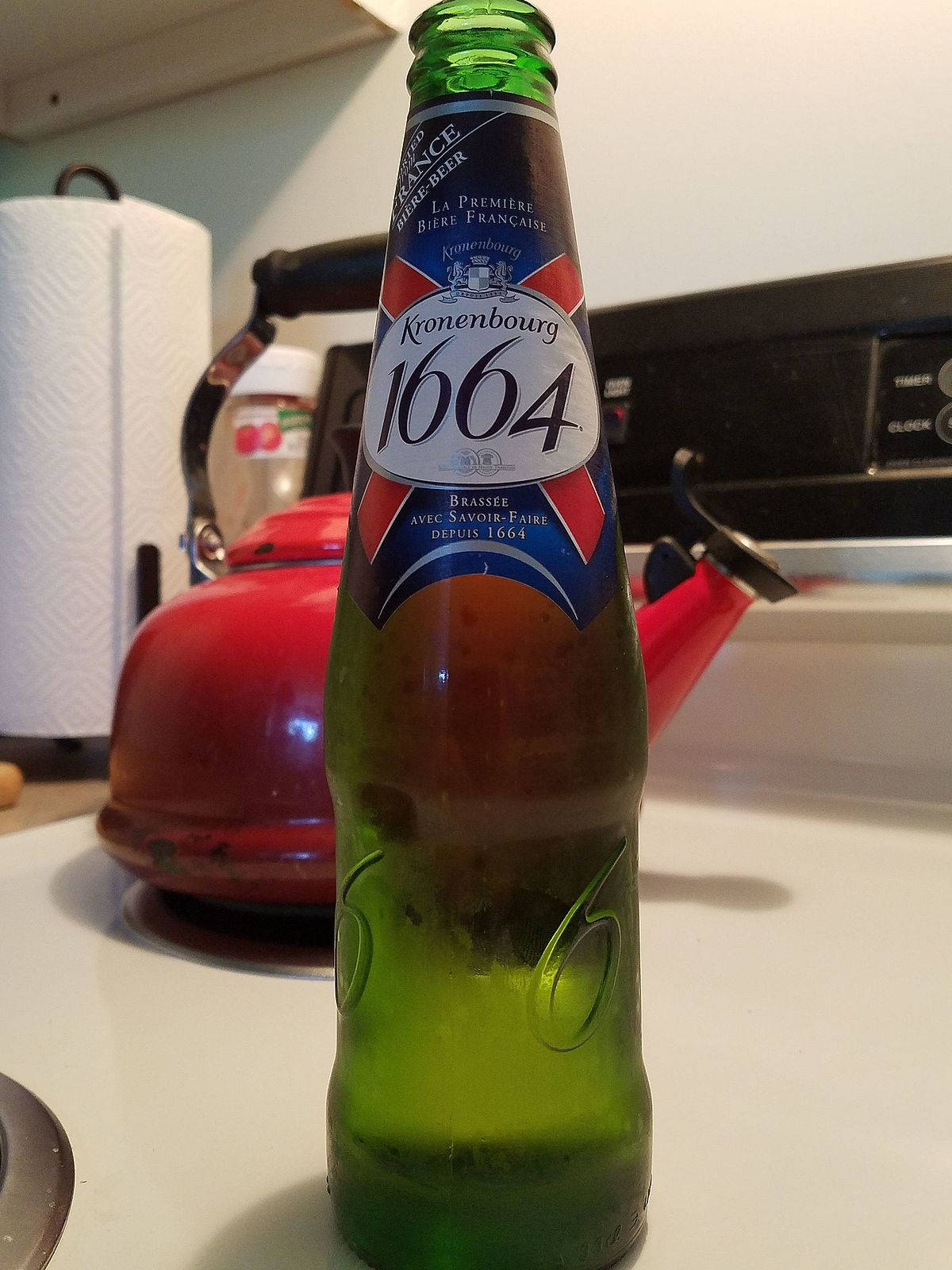 廚房枱上紅色水煲旁邊嘅綠色Kronenbourg 1664啤酒樽。