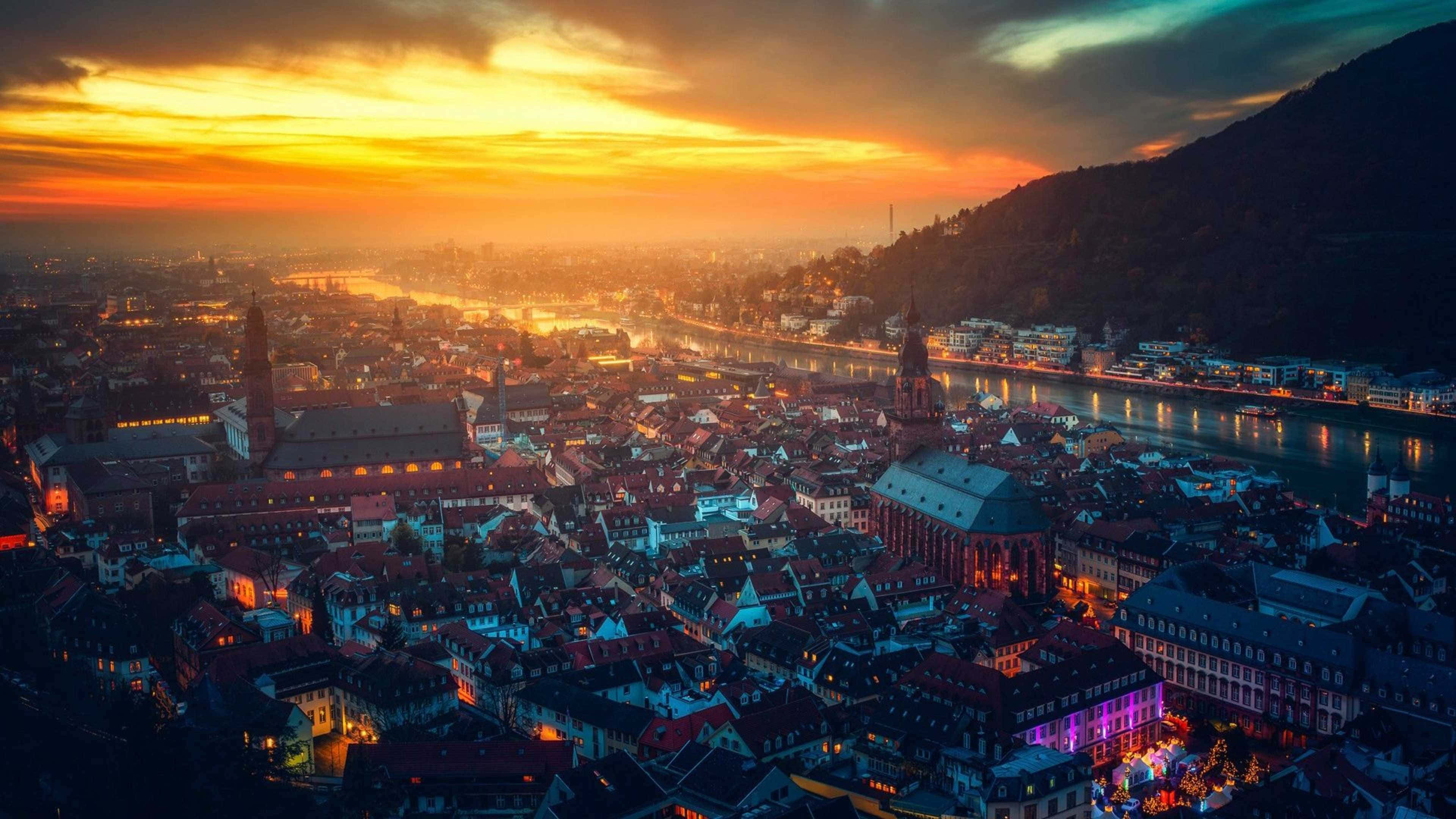 Germany 桌布 壁紙 — 歷史悠久的歐洲城市在日落時的鳥瞰圖，金色天空映照在河流和發光的屋頂上。