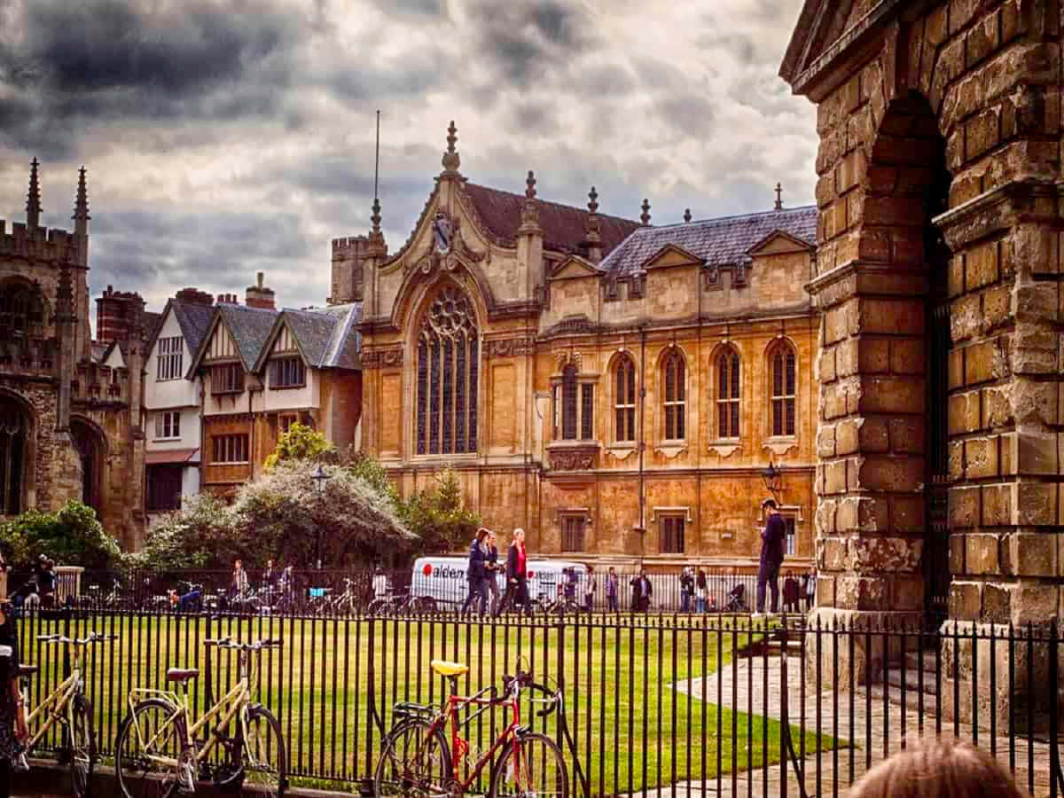 Oxford United Kingdom 桌布 壁紙 — 歷史悠久的石造大學庭院，哥德式建築，單車停泊在圍欄旁，人們在陰天行走。