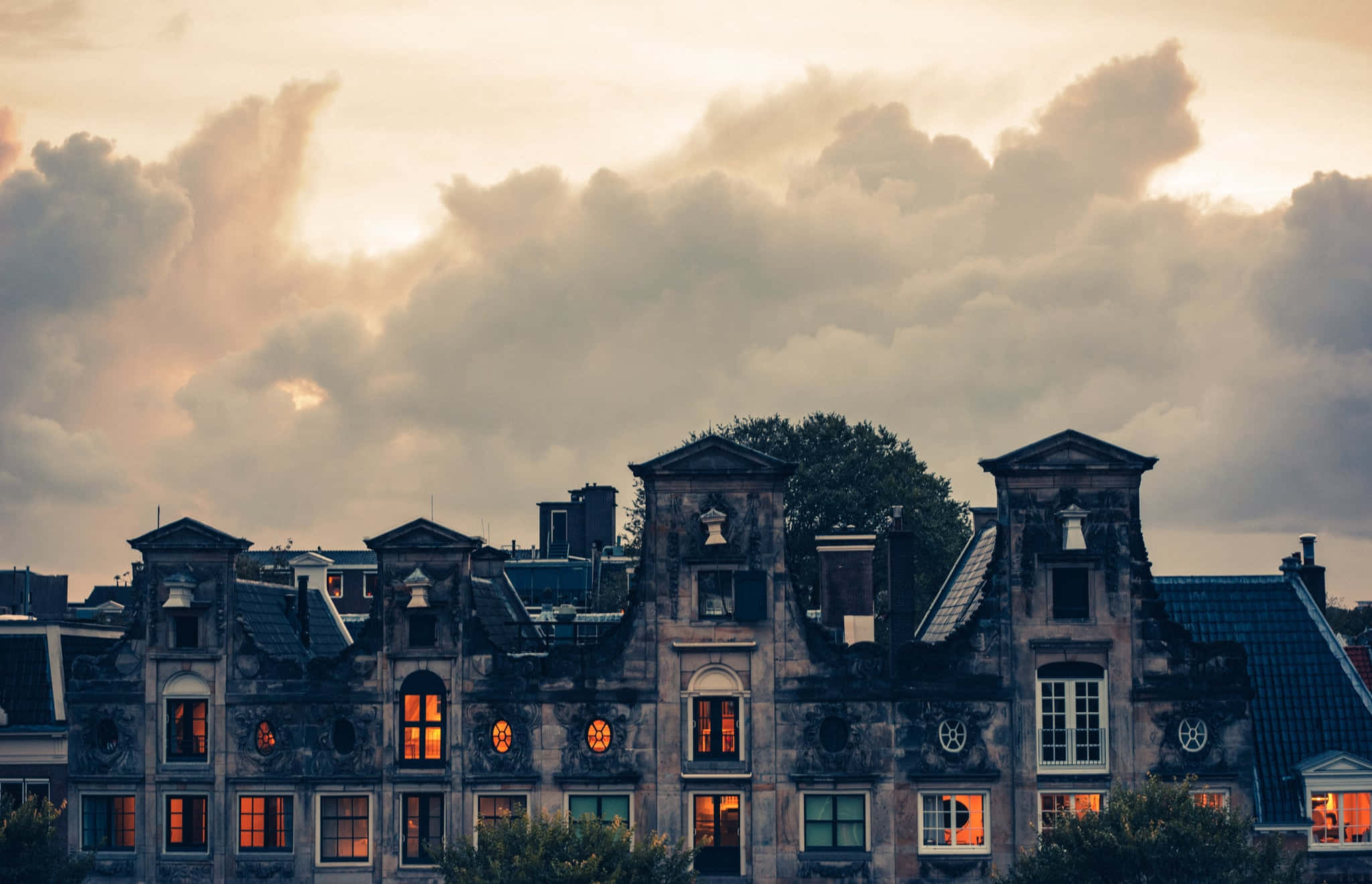 Haunted House 桌布 壁紙 — 歷史悠久的荷蘭運河房屋在戲劇性的暮色天空和柔軟雲朵的映襯下溫暖地發光。